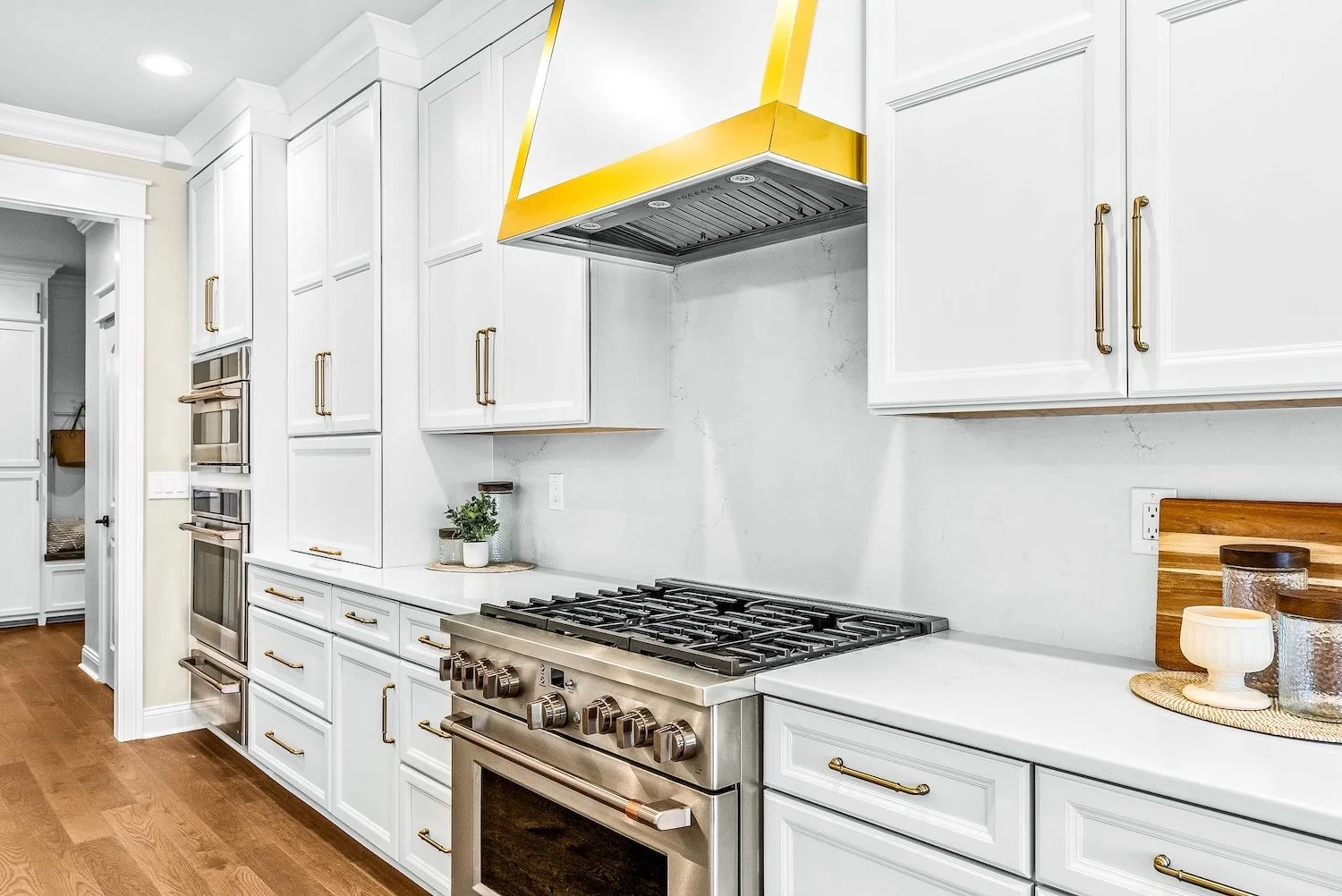 Modern kitchen with white cabinets, stainless steel stove, gold accents, and a yellow range hood.