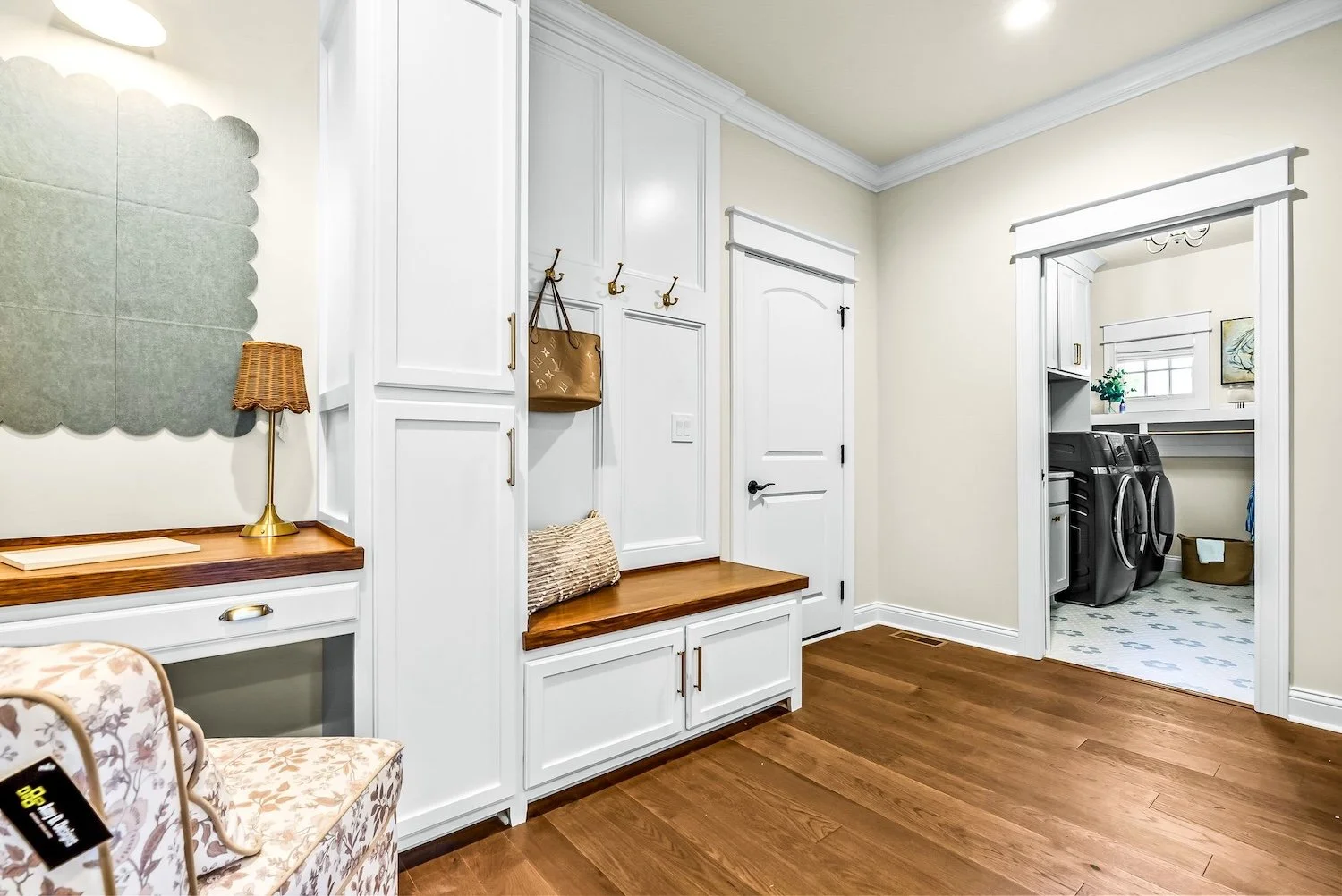 An entryway with white built-in cabinets, hooks with bags and a pillow, a wooden bench, a door, and a visible laundry room with washer and dryer.