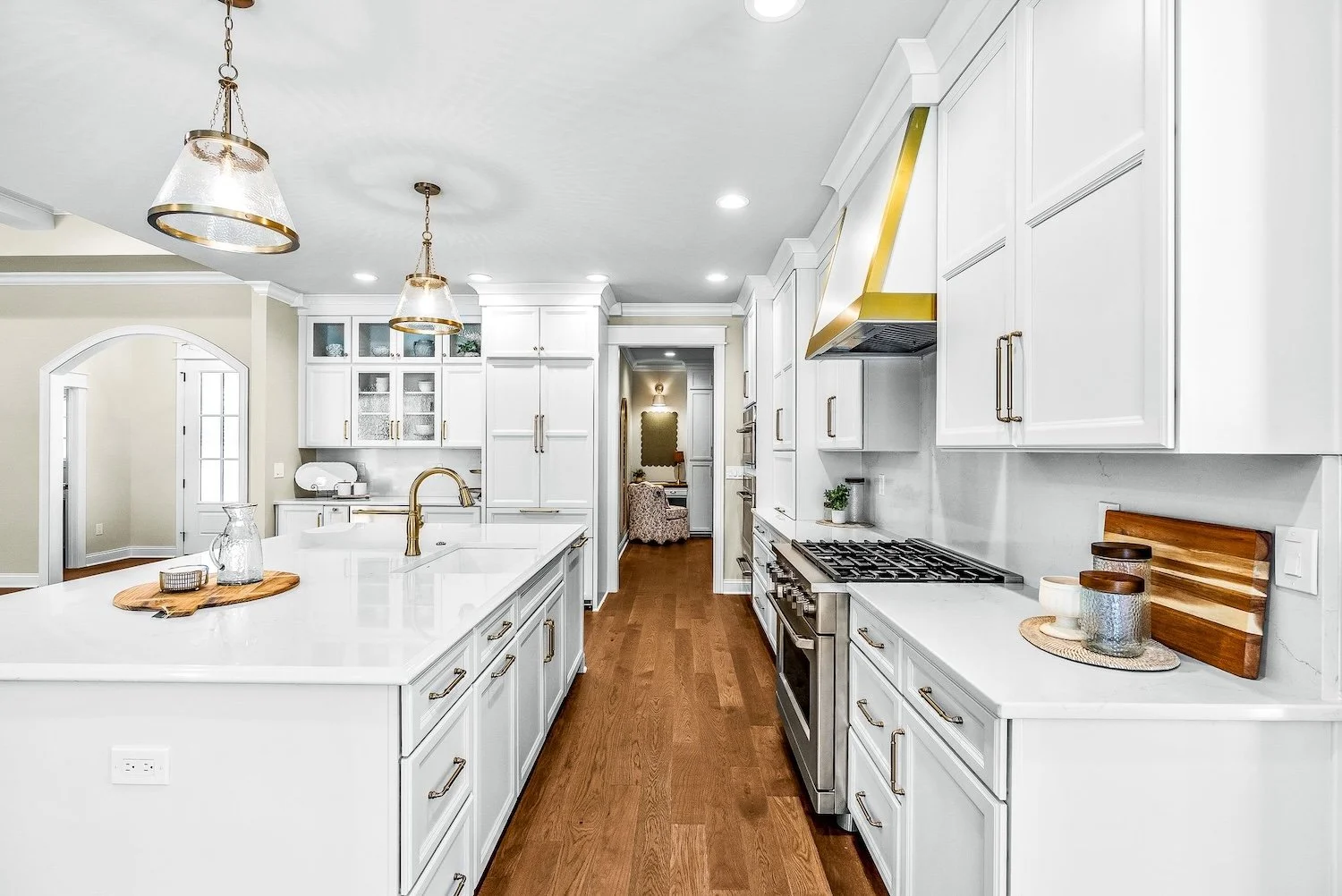 Modern white kitchen with gold accents, wood flooring, and a large kitchen island with a gold faucet.