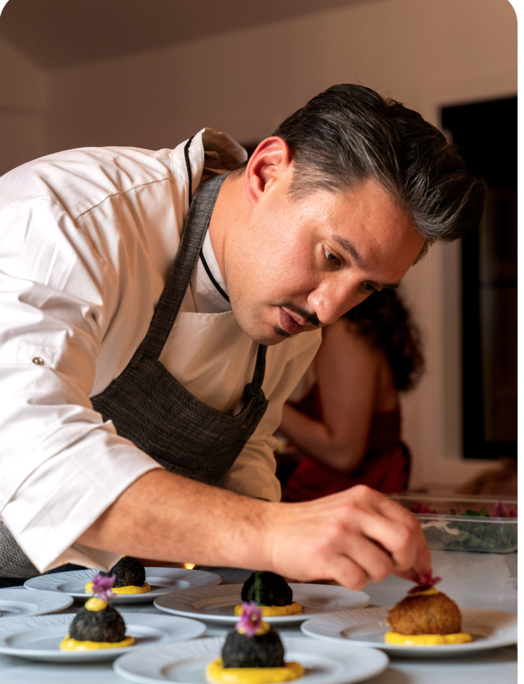 A chef garnishing plated savory appetizers with small edible flowers at a kitchen counter.