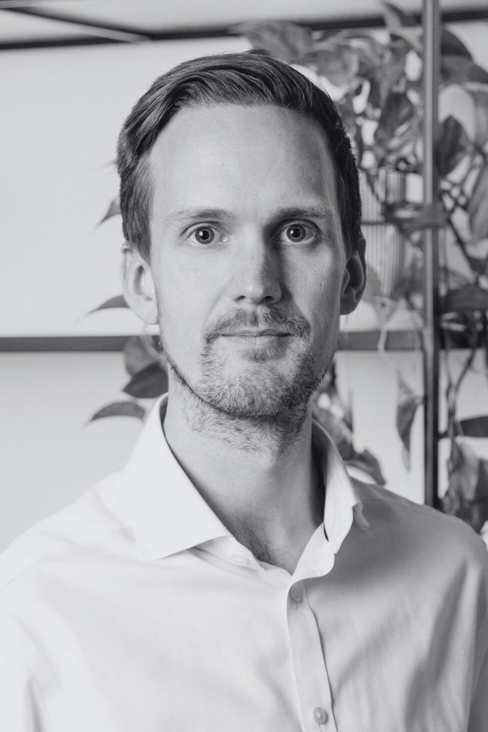 Black and white portrait of a Steve with short hair and a beard, smiling, with bookshelves in the background.