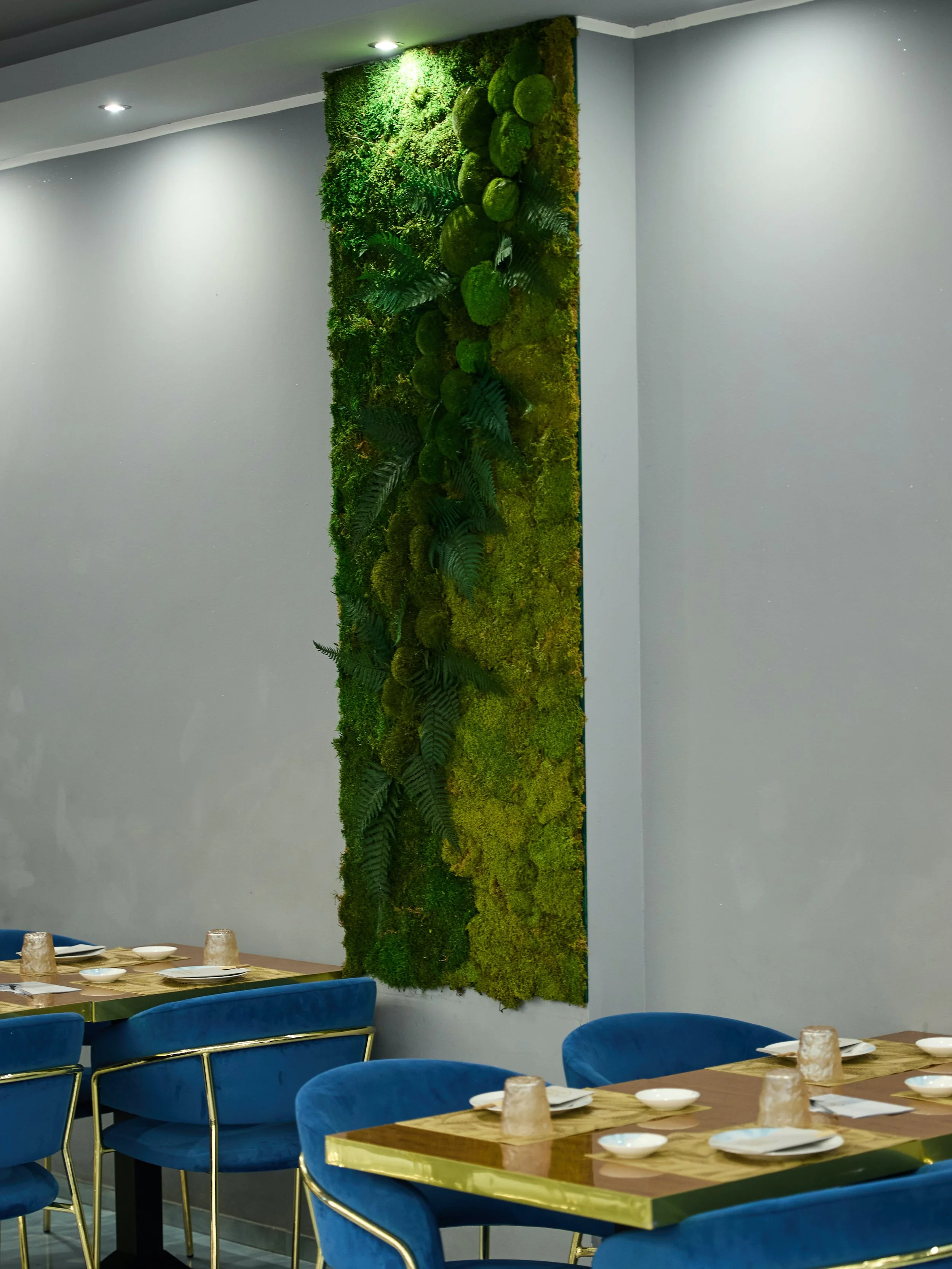 Parete decorata con un pannello di muschio e piante verdi in un ristorante con tavoli apparecchiati.