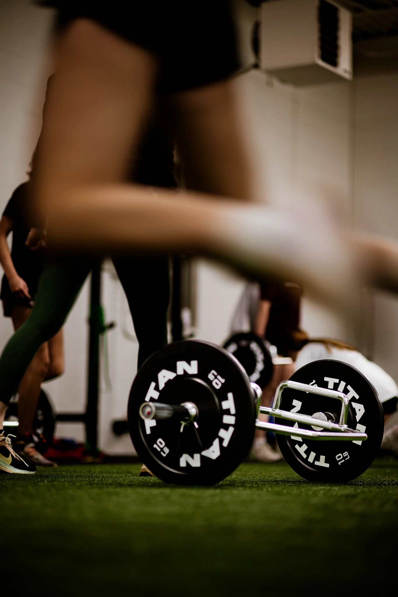 People participating in a workout session at an indoor gym, lifting kettlebells and barbells on artificial turf floor, a group of athletes preparing for exercise at Golden Sports Performance in the Applewood neighborhood of Lakewood, Colorado.