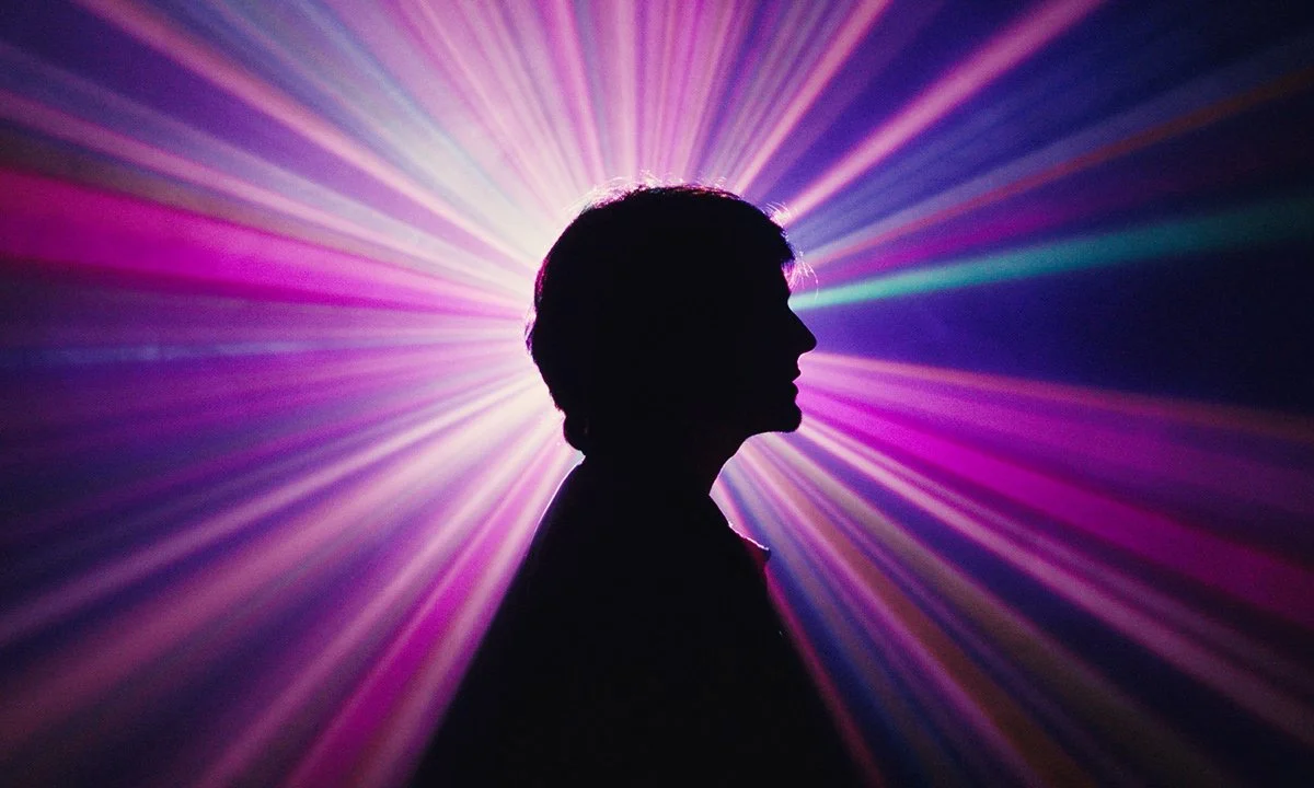 Silhouette of a person’s profile with colorful light beams radiating behind them.