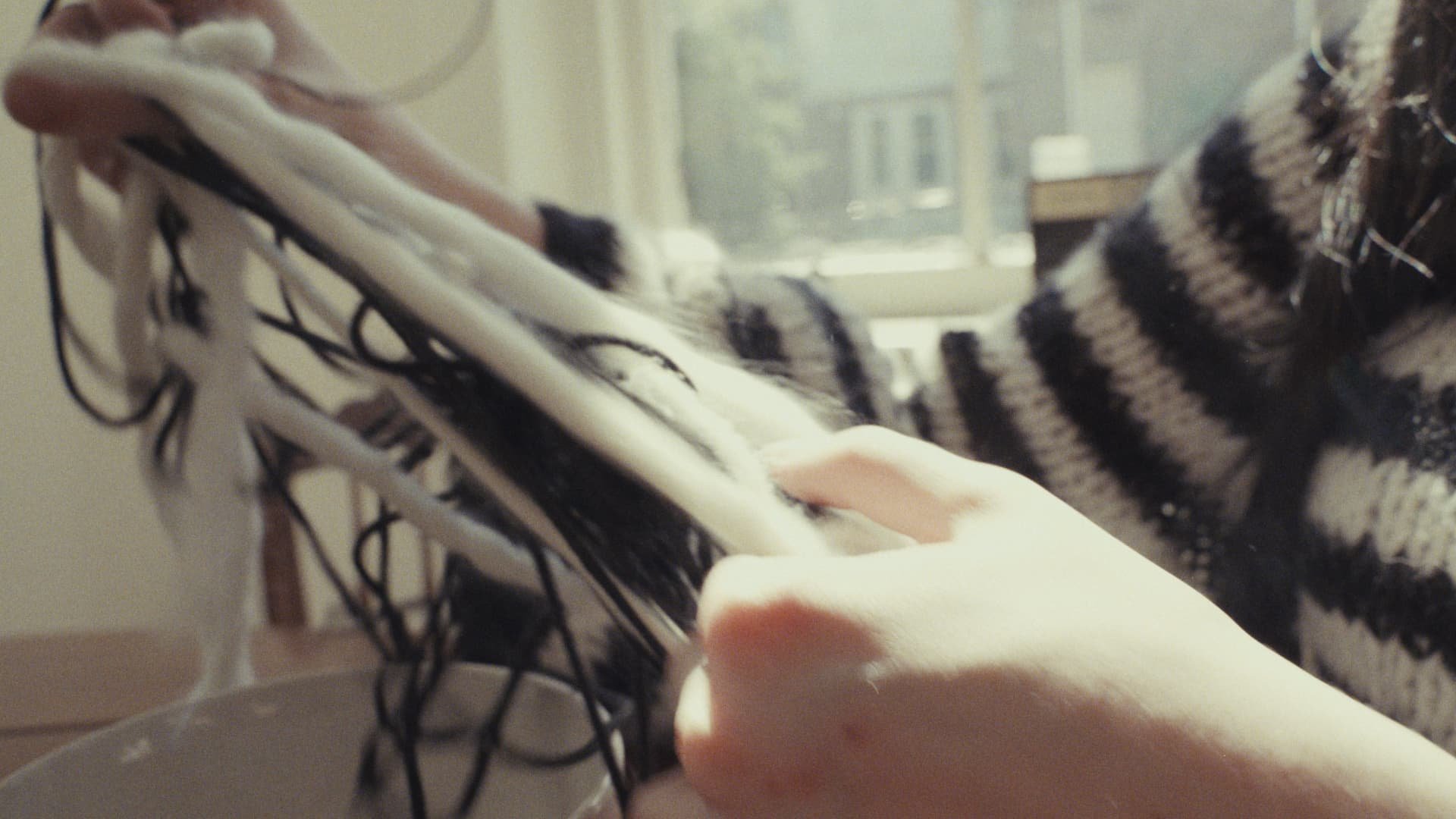 Person holds a black and white embroidered hat or piece of fabric near a window, with a striped sweater visible in the background.