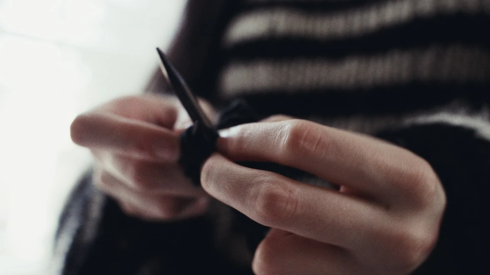 Close-up of a person's hand knitting with black yarn using knitting needles.