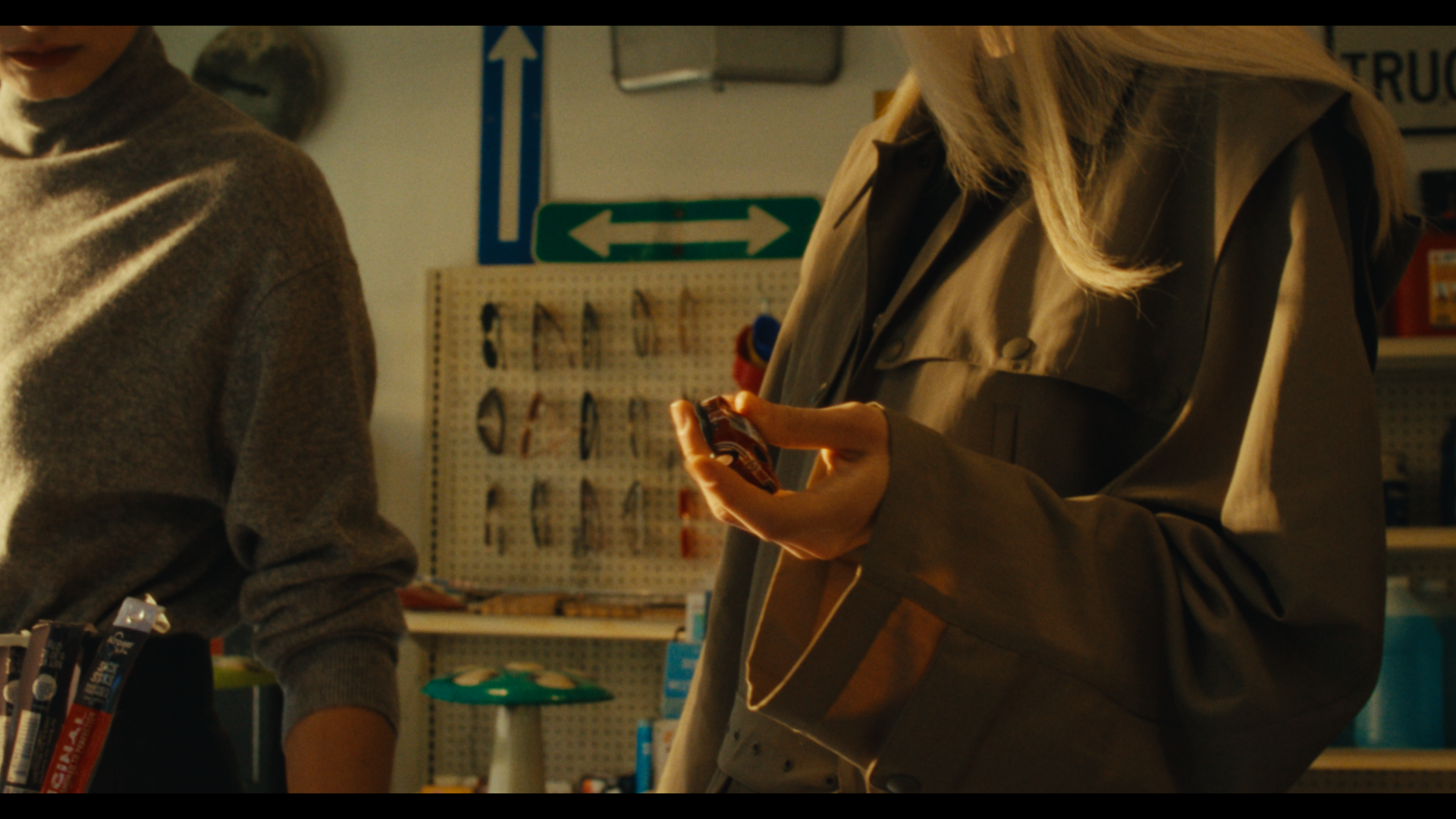 A person in a beige trench coat holding a small object in their hand inside a store with various tools on display.