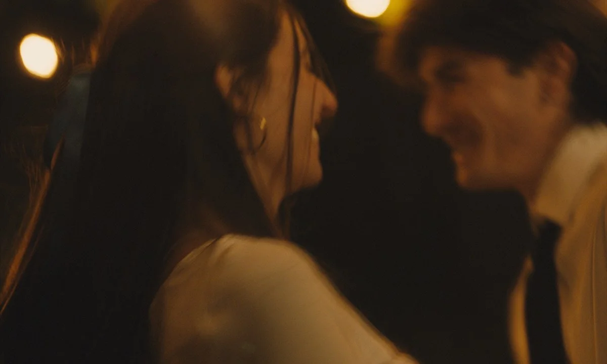 A romantic scene with a woman and a man smiling close to each other at night with blurred lights in the background.