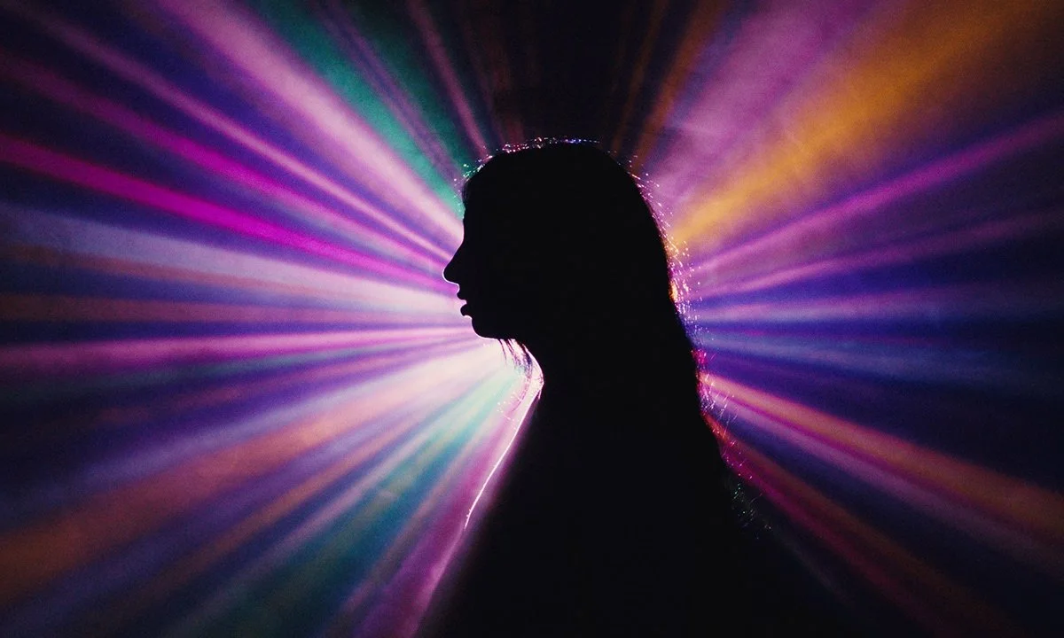Silhouette of a woman's profile against colorful, radiant light beams in the background.
