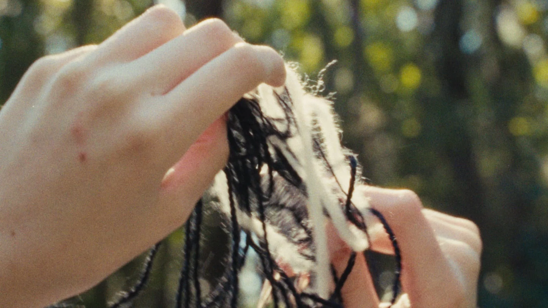 Close-up of a person's hands holding a wet towel with black and white threads, with a blurred background of trees and sunlight.