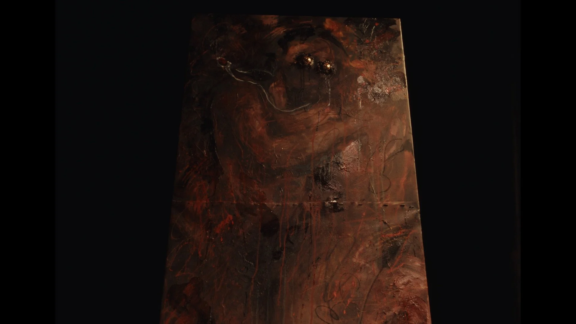 An abstract painting with dark red, black, and metallic colors, featuring a face-like figure with shiny gold eyes.