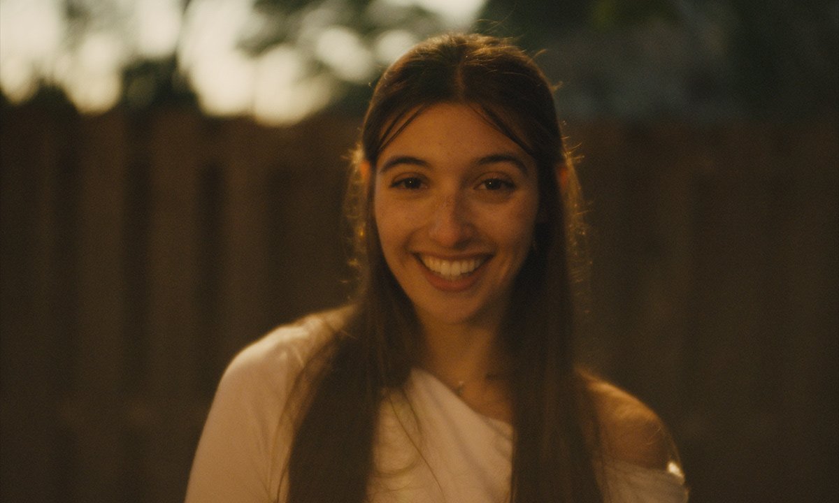 A young woman with long dark hair smiling outdoors during sunset.