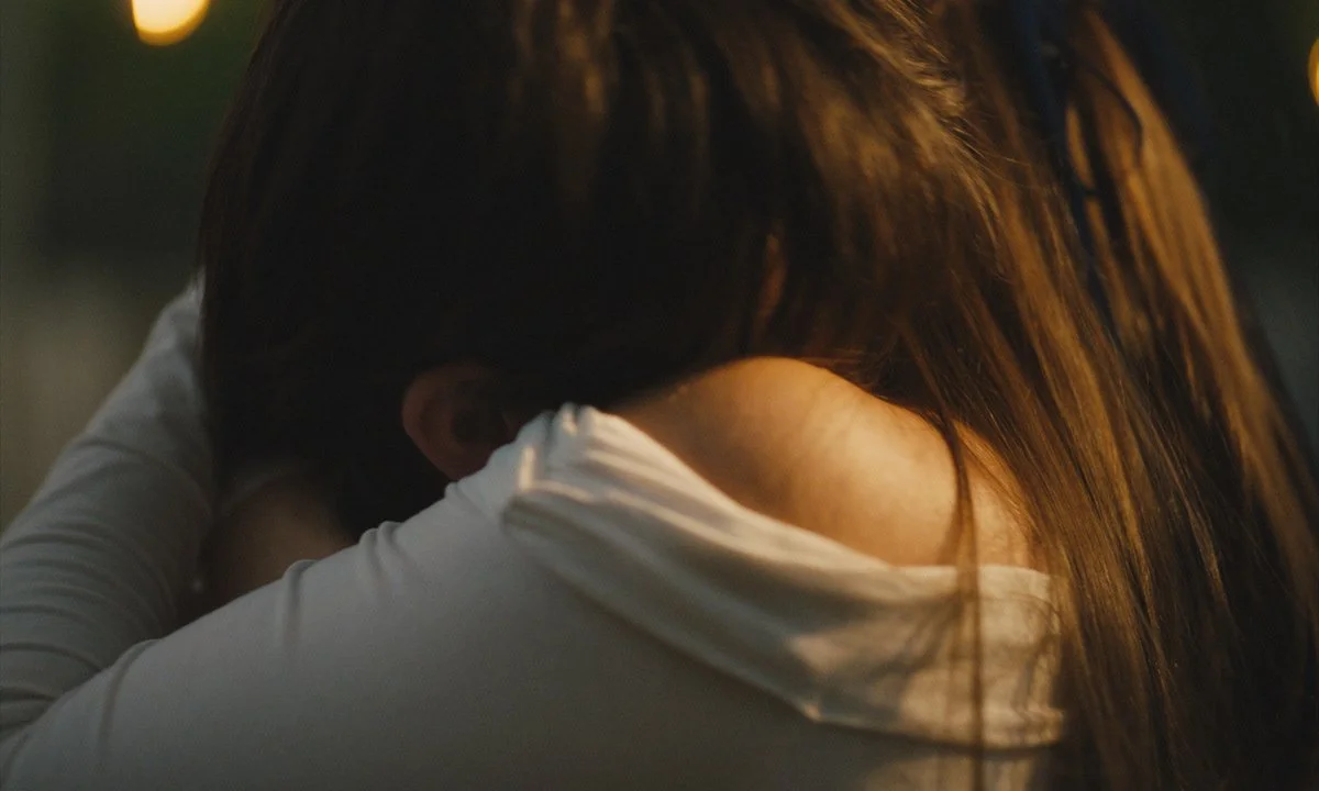 Two people hugging each other, one has long brown hair and the other has shorter dark hair, in an emotional embrace.