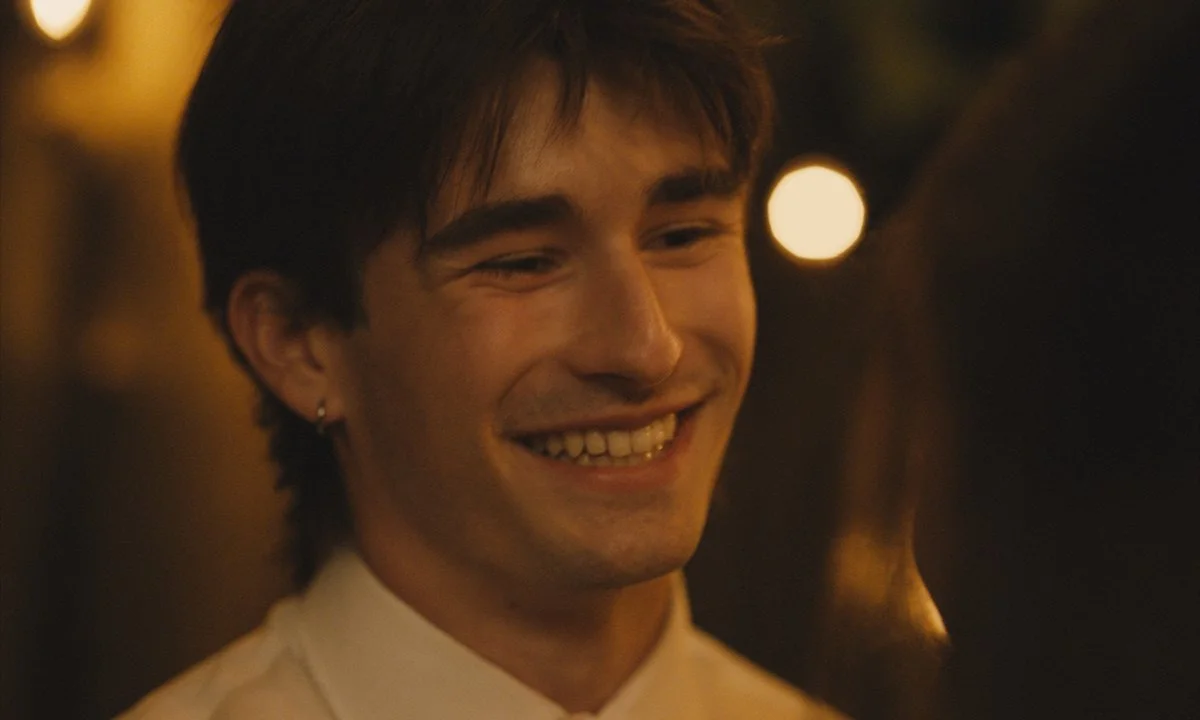 A young man with short dark hair and an earring, smiling in a warmly lit setting.