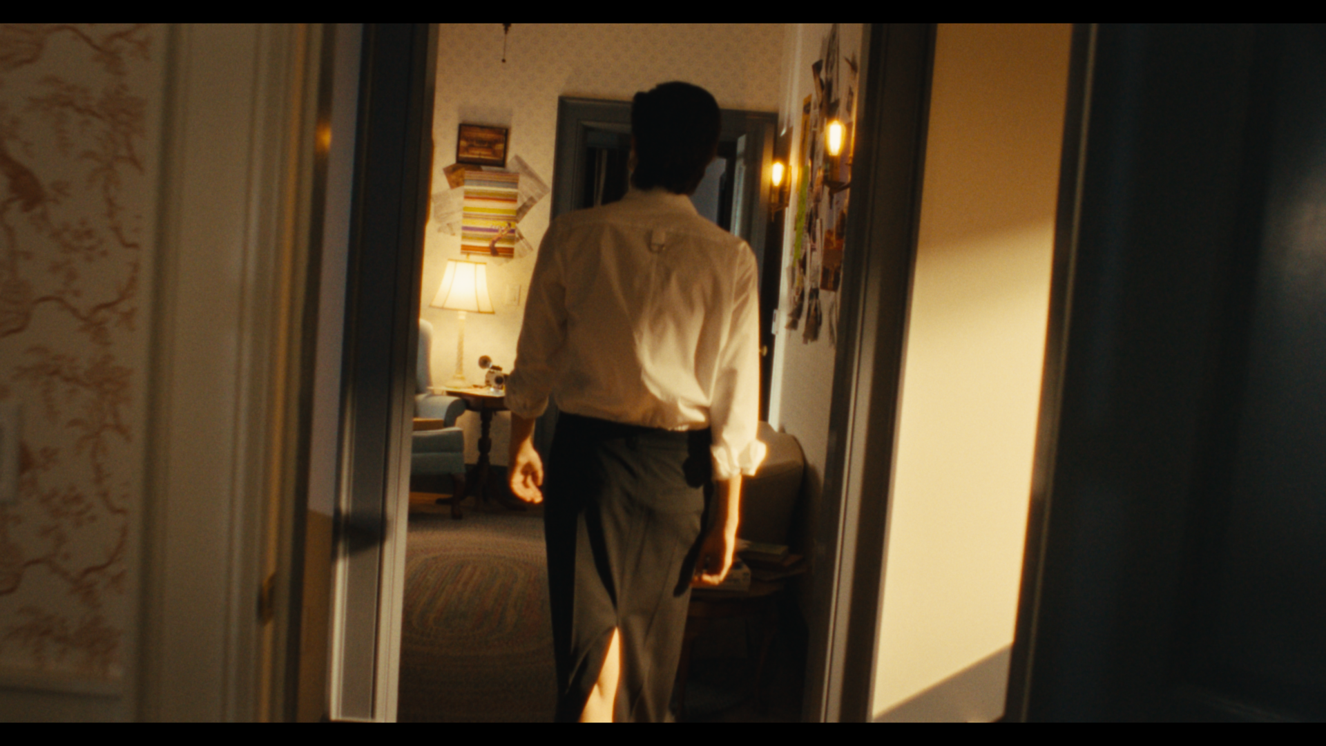 A person walking through a doorway into a warmly lit room with a lamp and artwork on the walls.