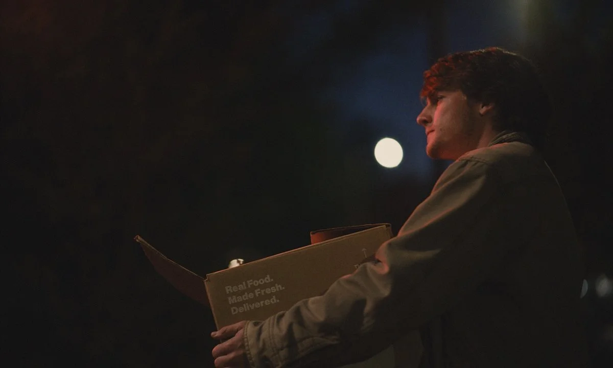 Young man holding a pizza box, illuminated by moonlight at night.
