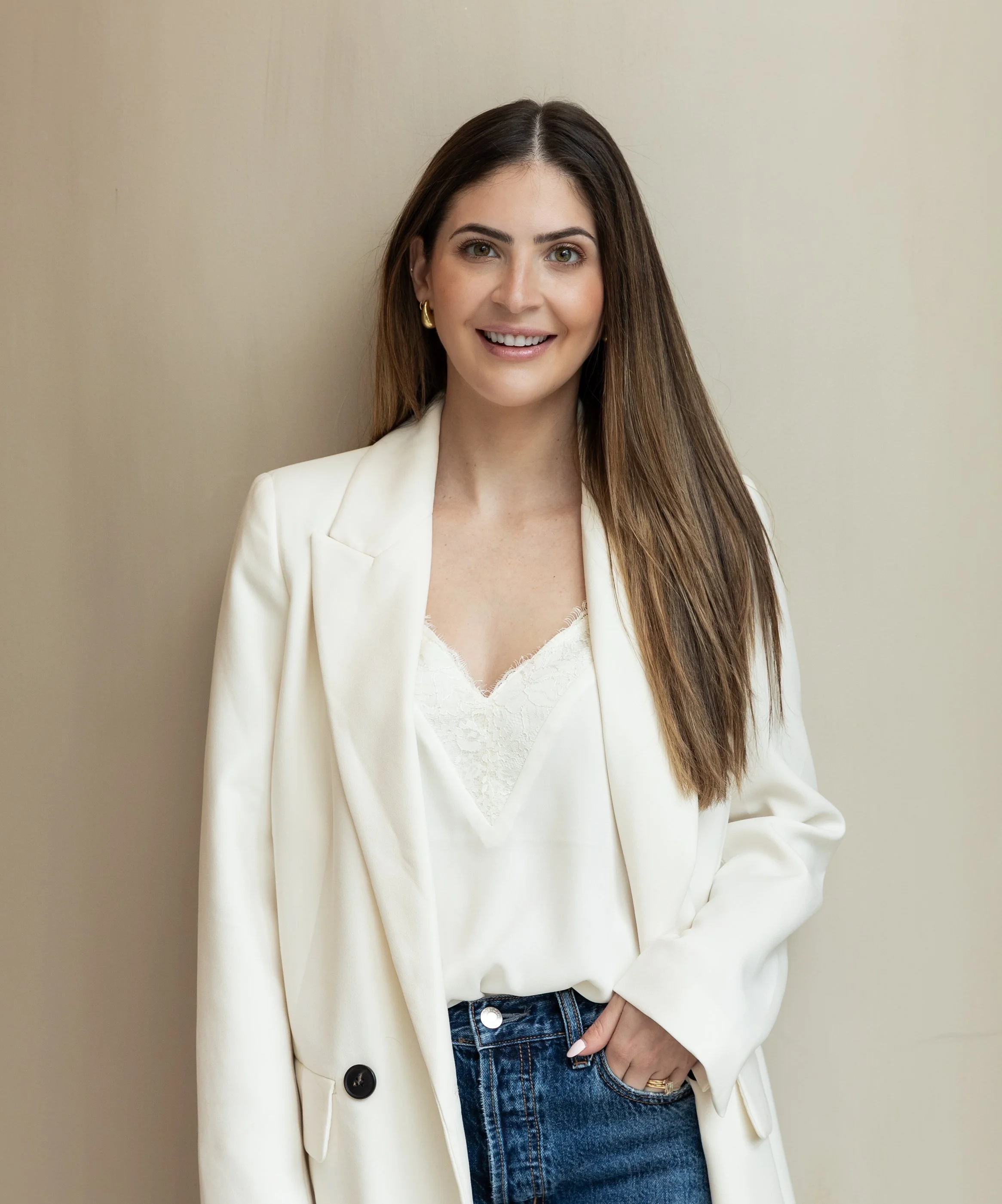 Woman in white blazer posing against a neutral background