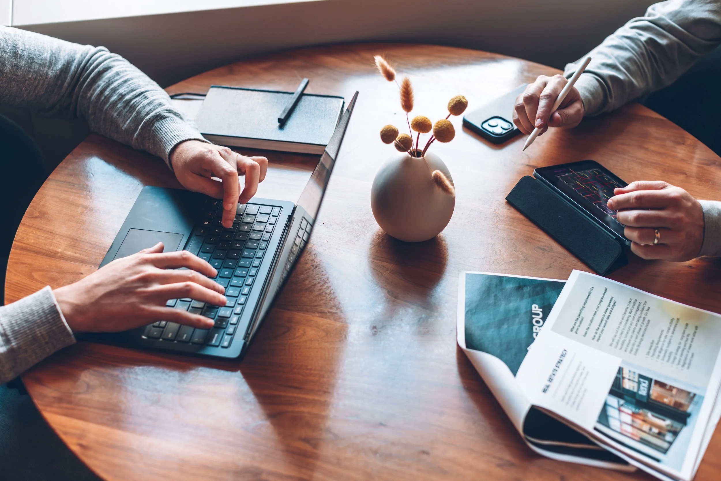 Two O’Leary Group team members working at a table with a laptop and iPad, reviewing a presentation deck.