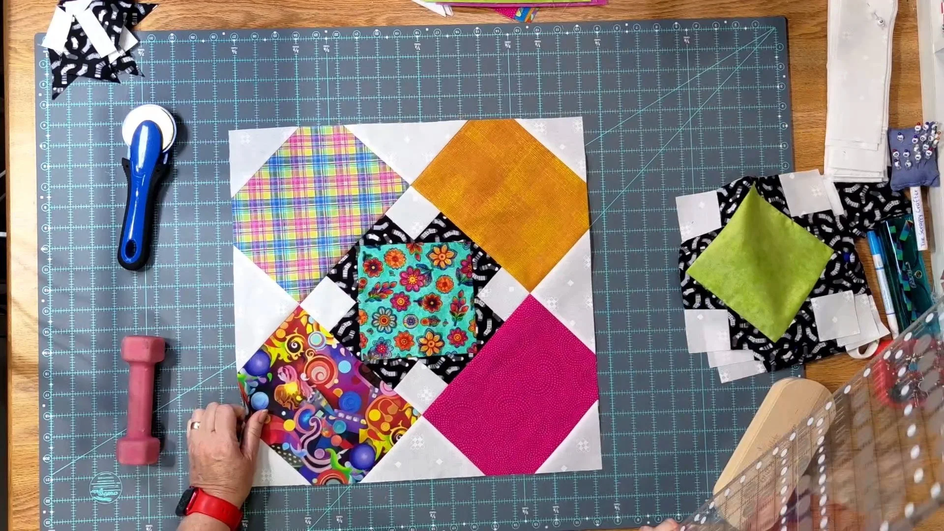 April’s completed Kitchen Sink quilt block with a floral center and pink, gold, plaid, and multicolored fabric on a cutting mat.