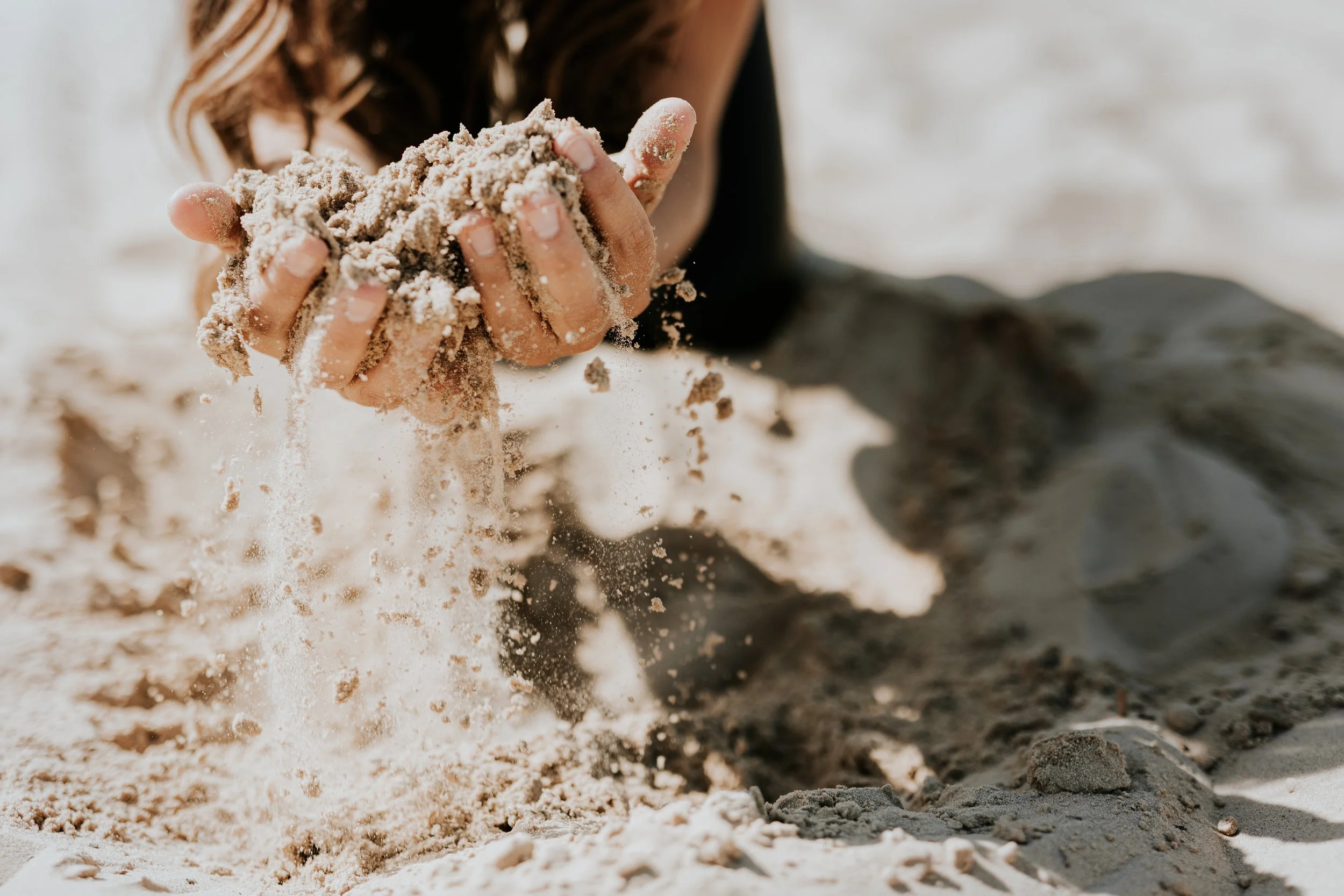 Een persoon die met hun hand zand op een strand oppakt en omhoog gooit.