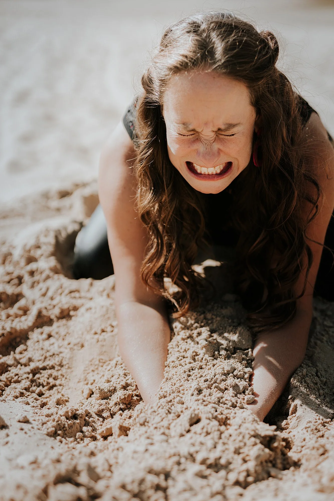 Een vrouw die in zand ligt met haar gezicht vertrokken door pijn of frustratie.