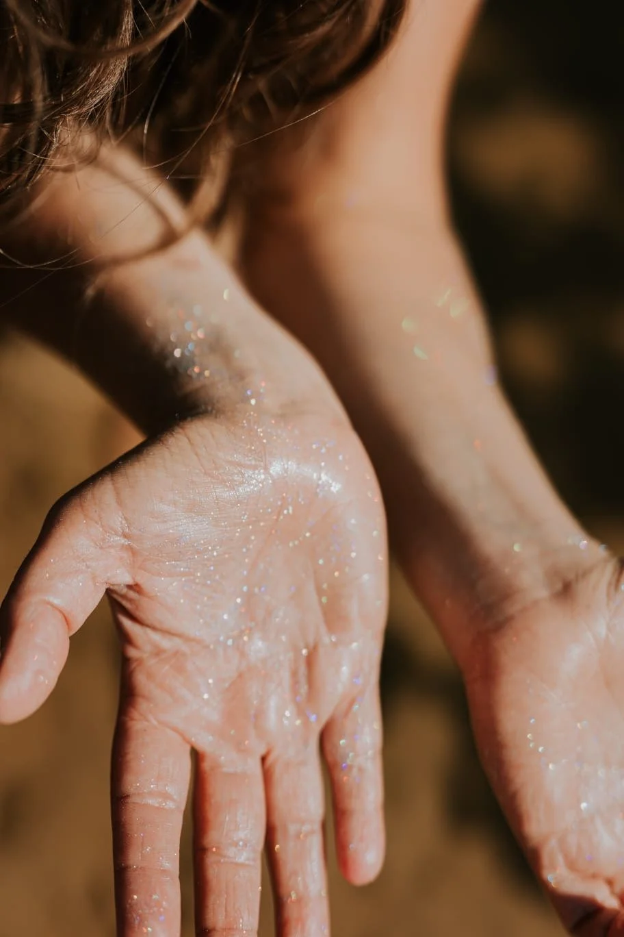 Close-up van een hand met glitter op de huid, met een veys in de achtergrond.