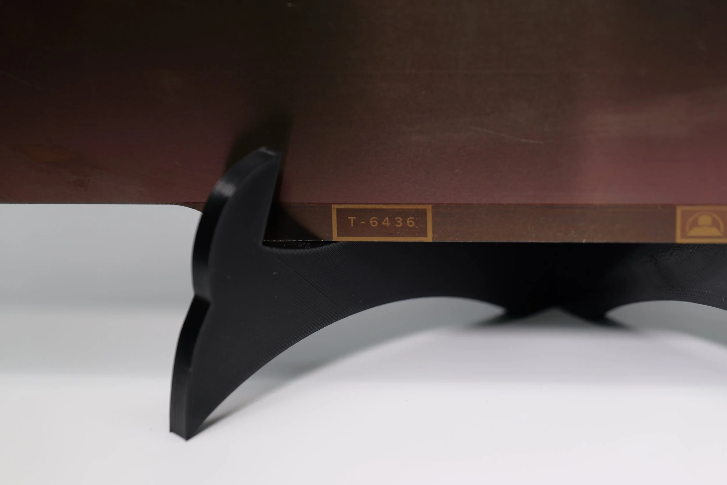 Close-up of a wooden object with a label 'T-6436' and a black curved support underneath.