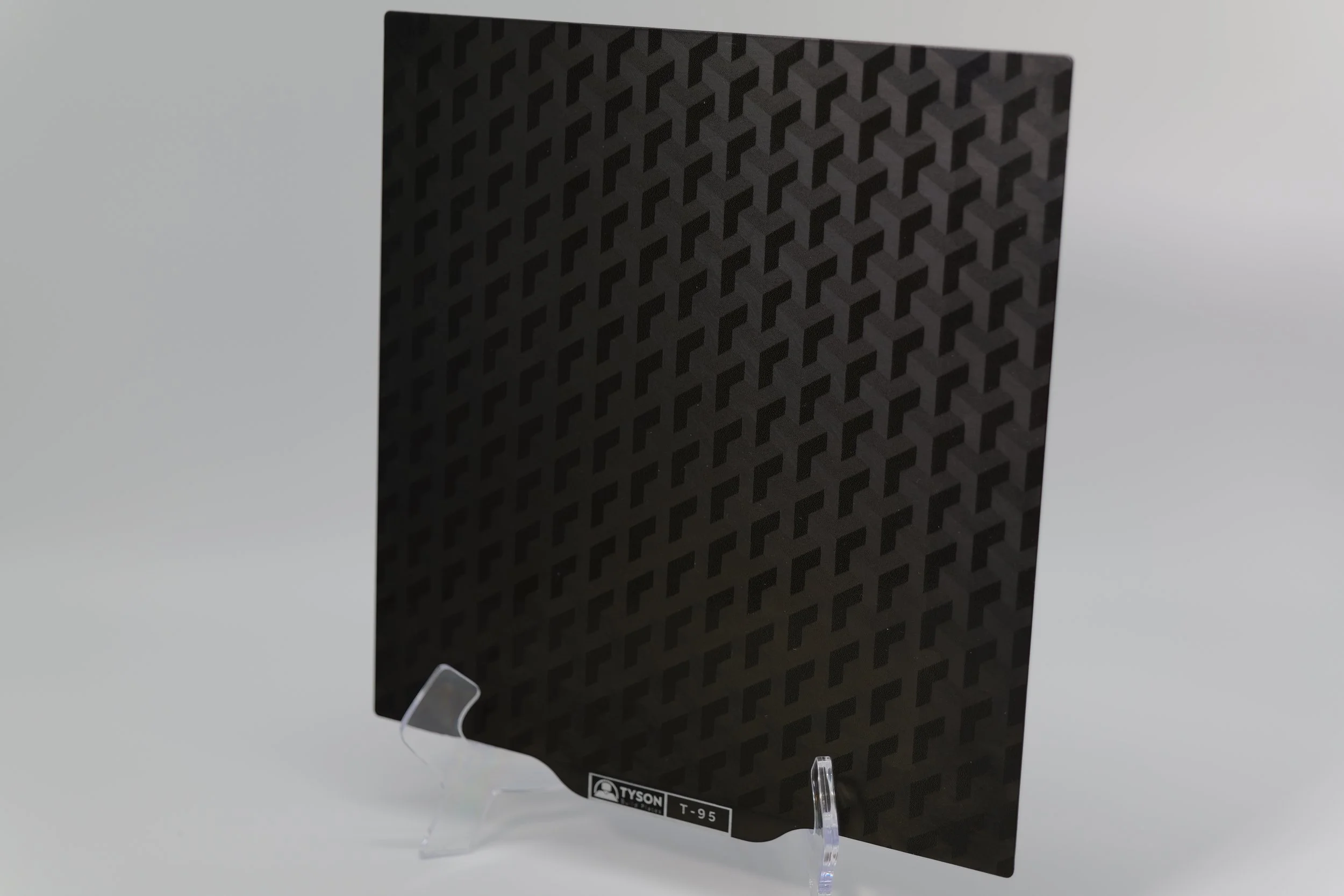 A piece of dark patterned paper with a geometric design, standing upright on a clear acrylic display stand.