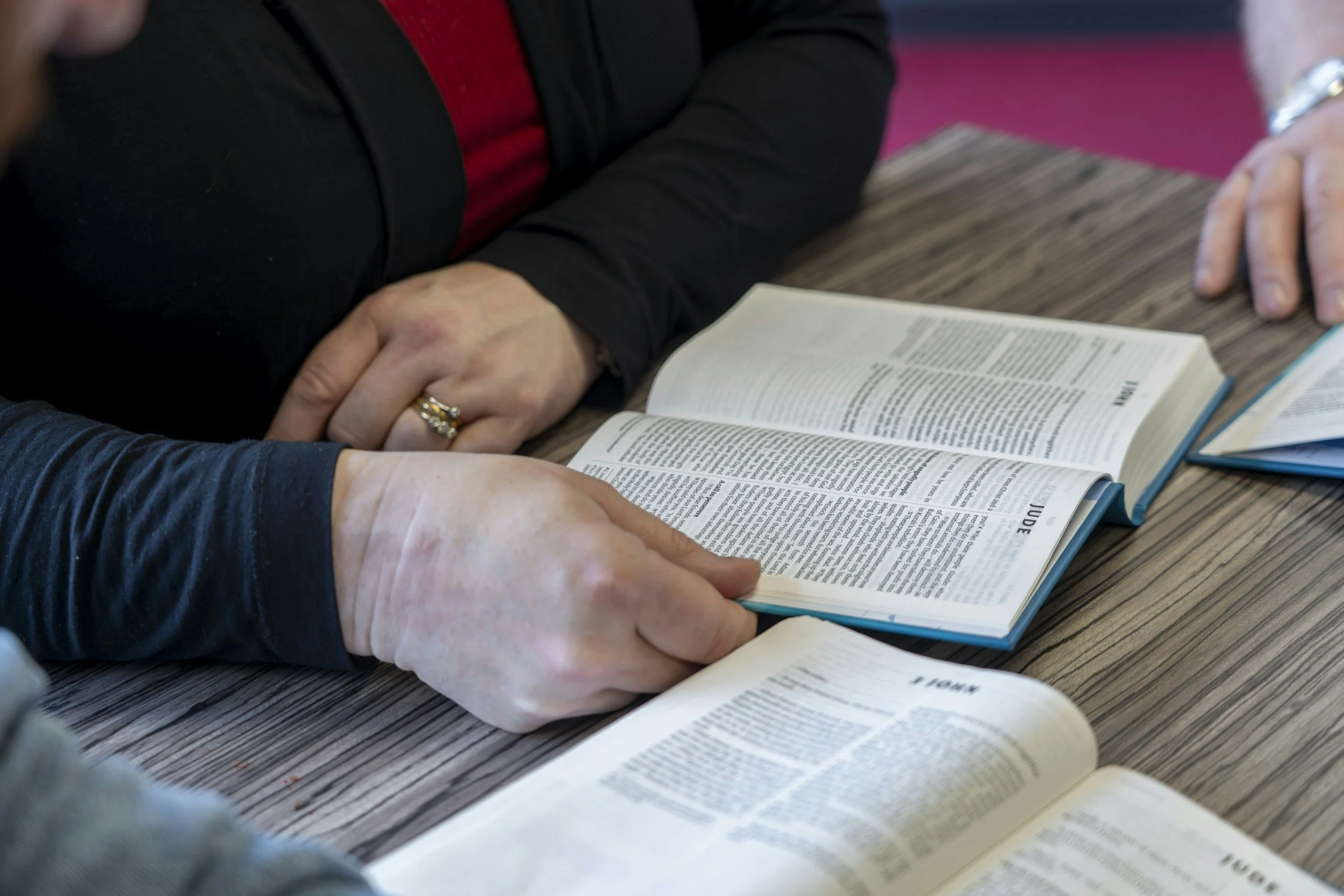 People reading and pointing at open books on a table.