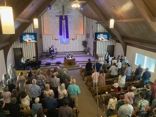 People gathered inside a church for a service, with an altar at the front and a congregation standing and sitting.