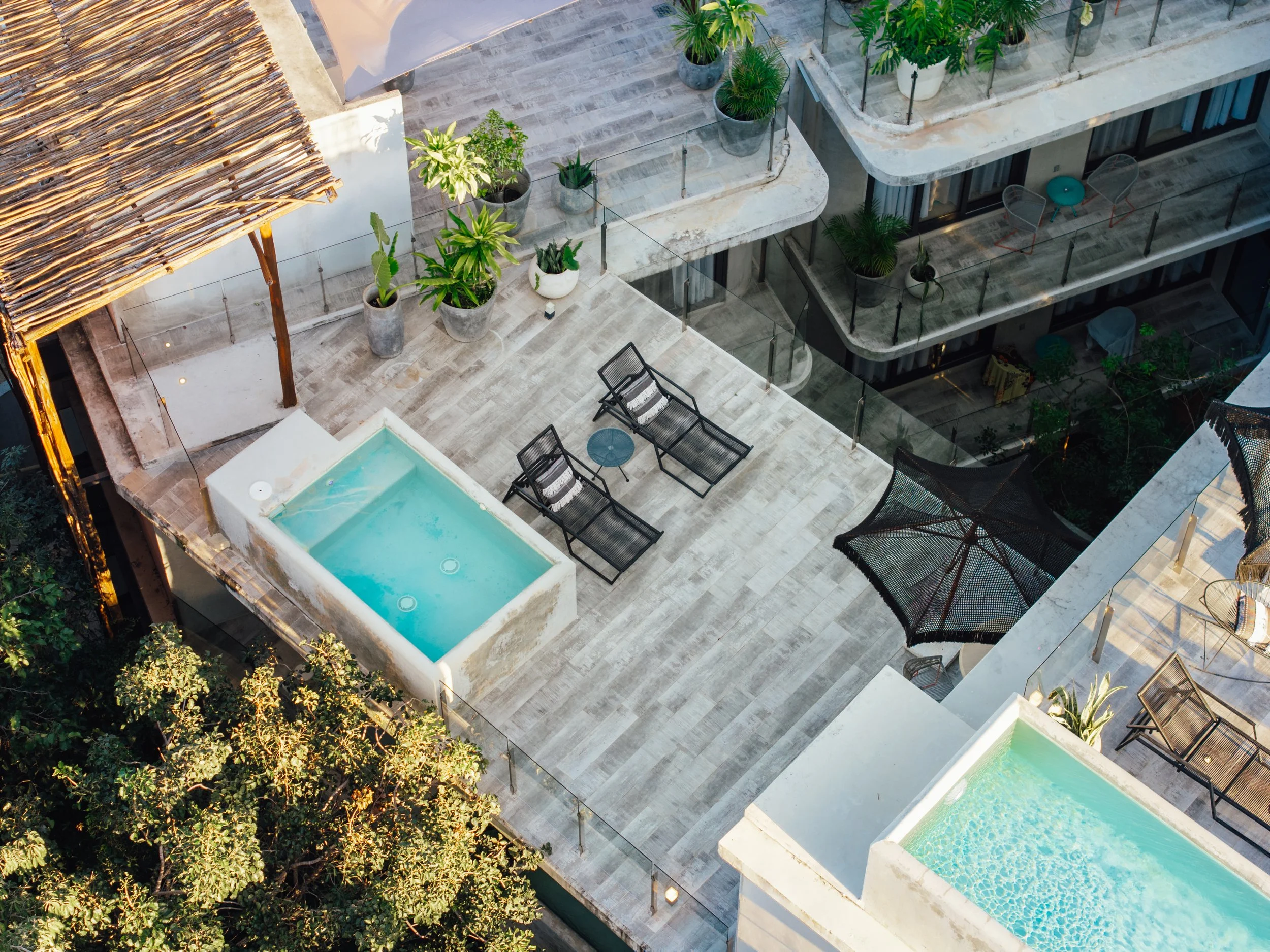 Aerial view of a modern balcony with potted plants, lounge chairs, and two small pools.