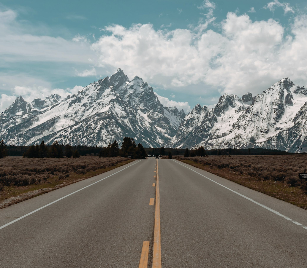 Open road leading to snow-capped mountains under a partly cloudy sky.