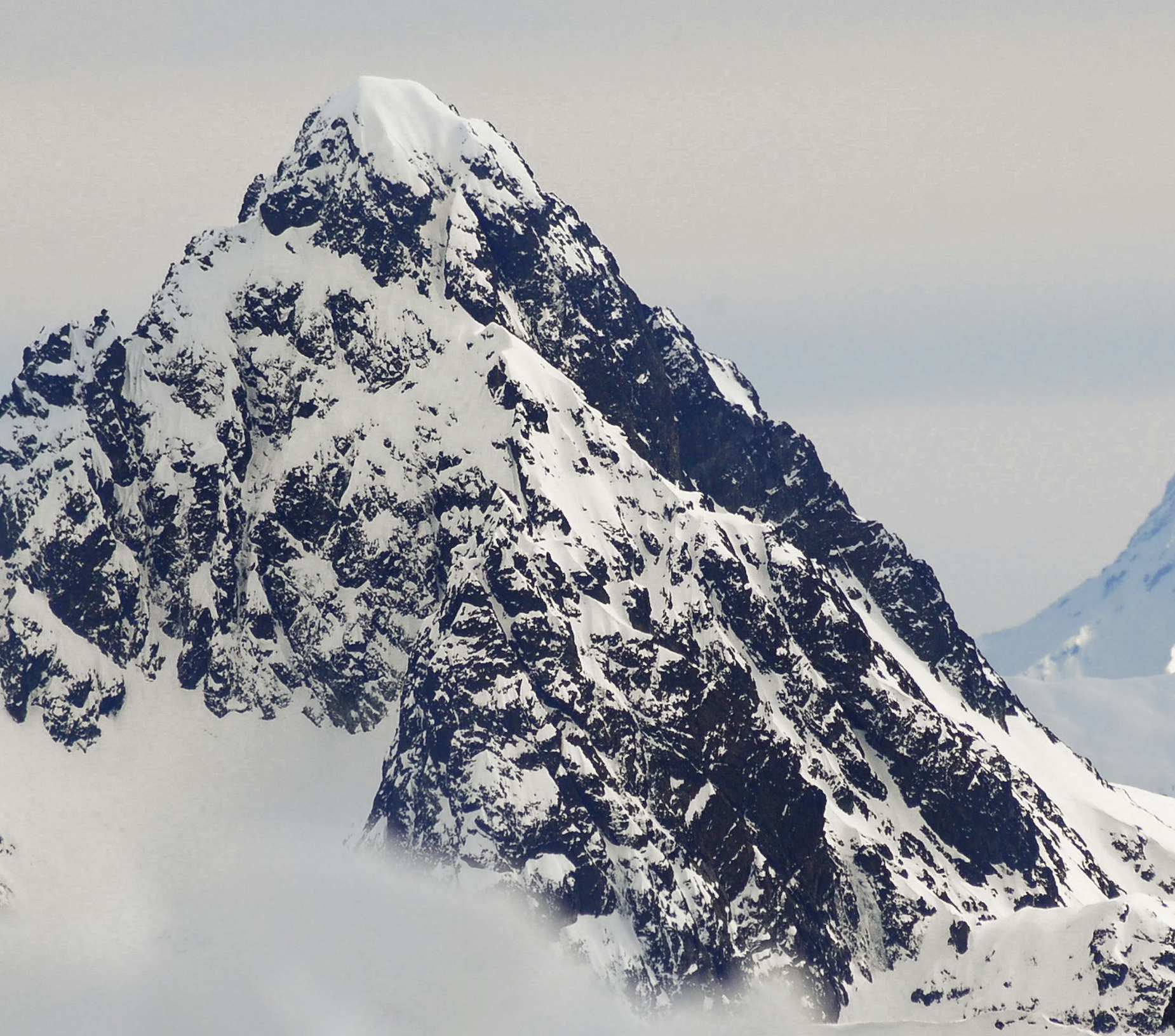 Snow-covered mountain peak with rugged rock formations against a cloudy sky