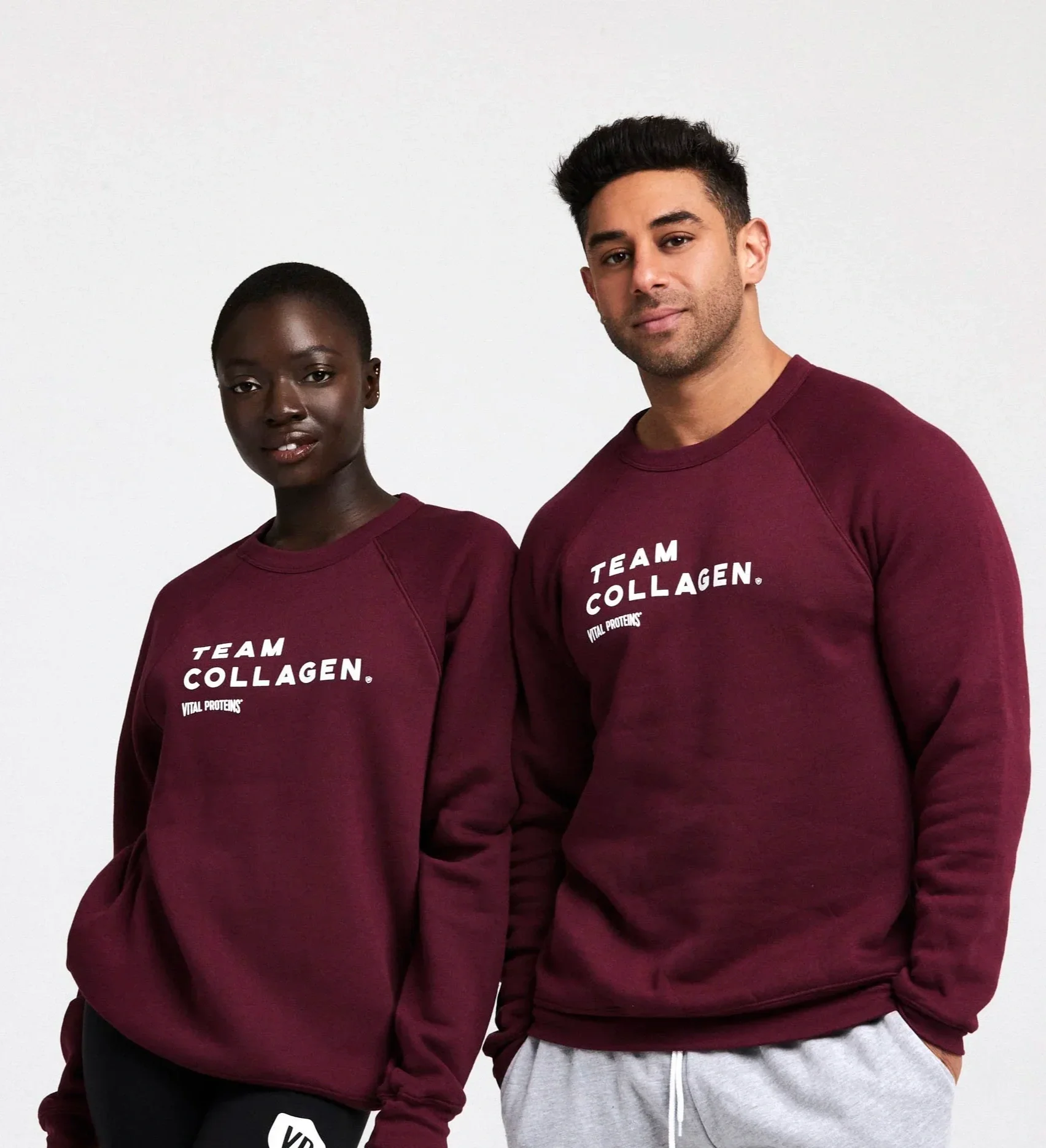 Two young adults, one woman and one man, standing side by side against a plain white background, wearing matching maroon sweatshirts with the words "TEAM COLLAGEN" printed on them.