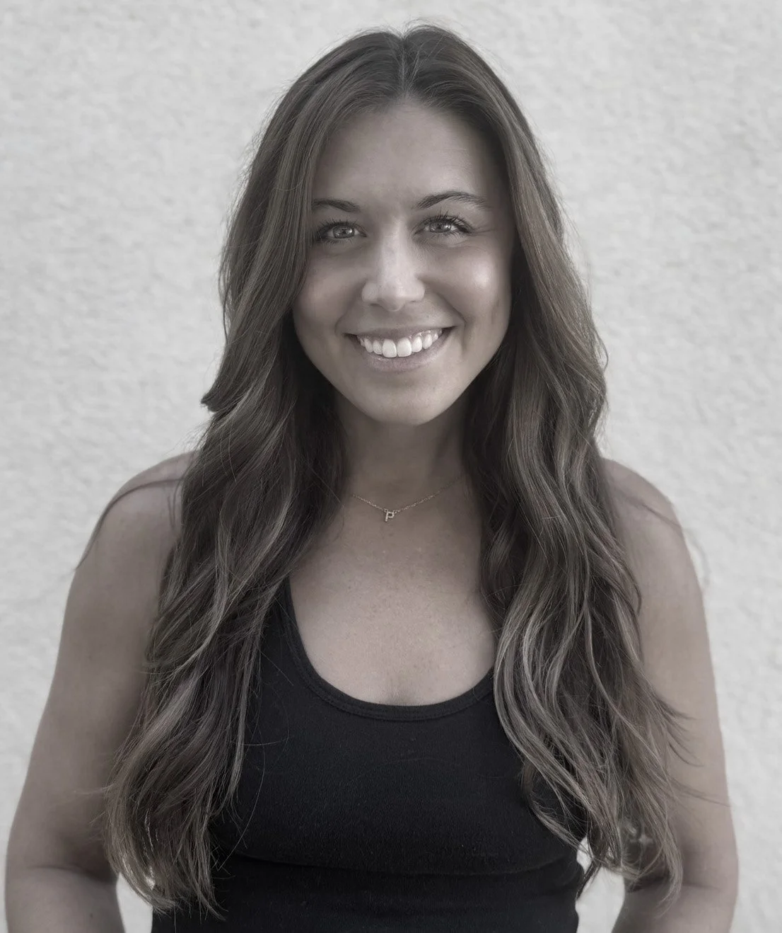 A woman with long wavy brown hair smiling in front of a neutral background.