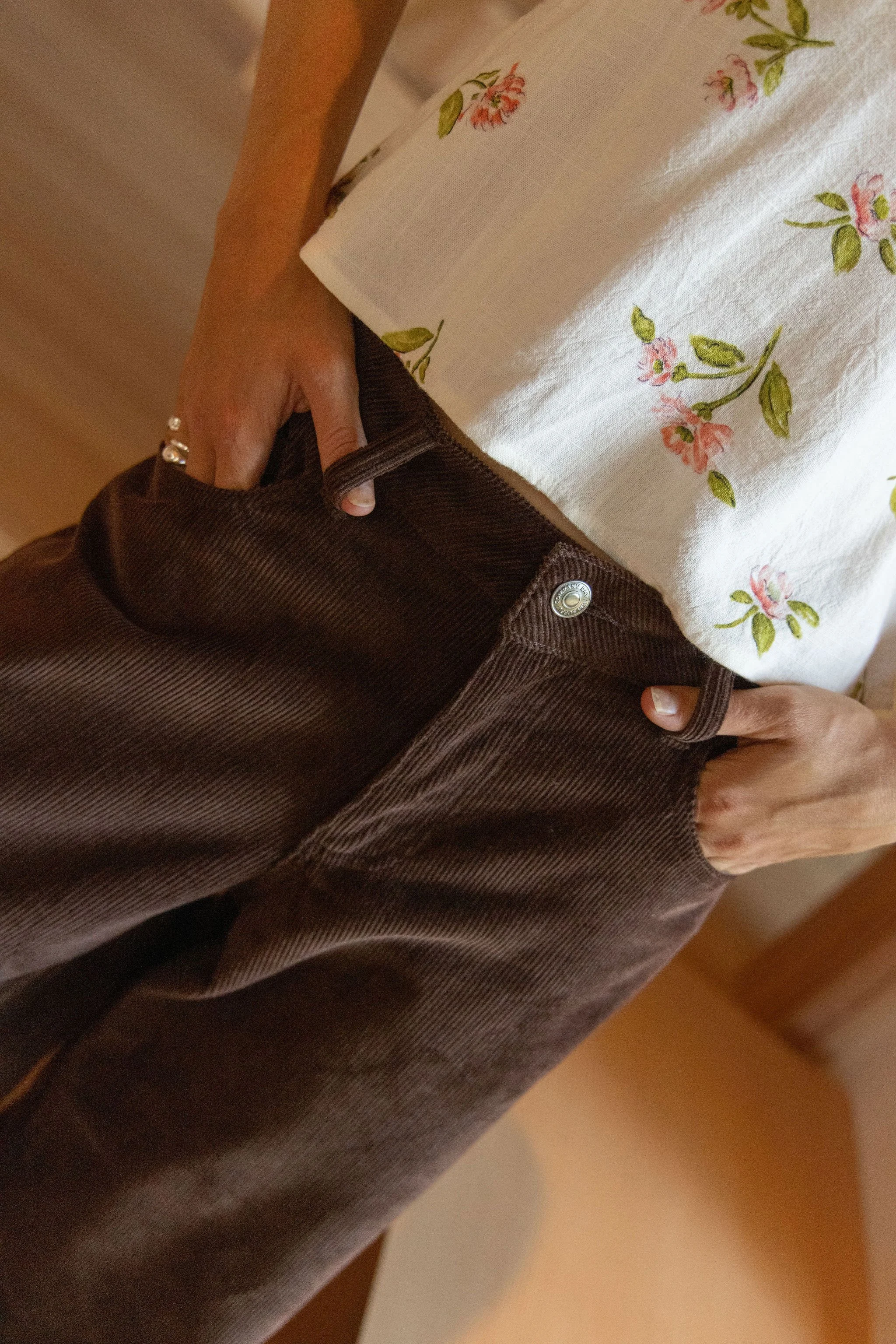 Close-up of a person wearing a white shirt with pink and green floral patterns, holding a brown cable-knit sweater.
