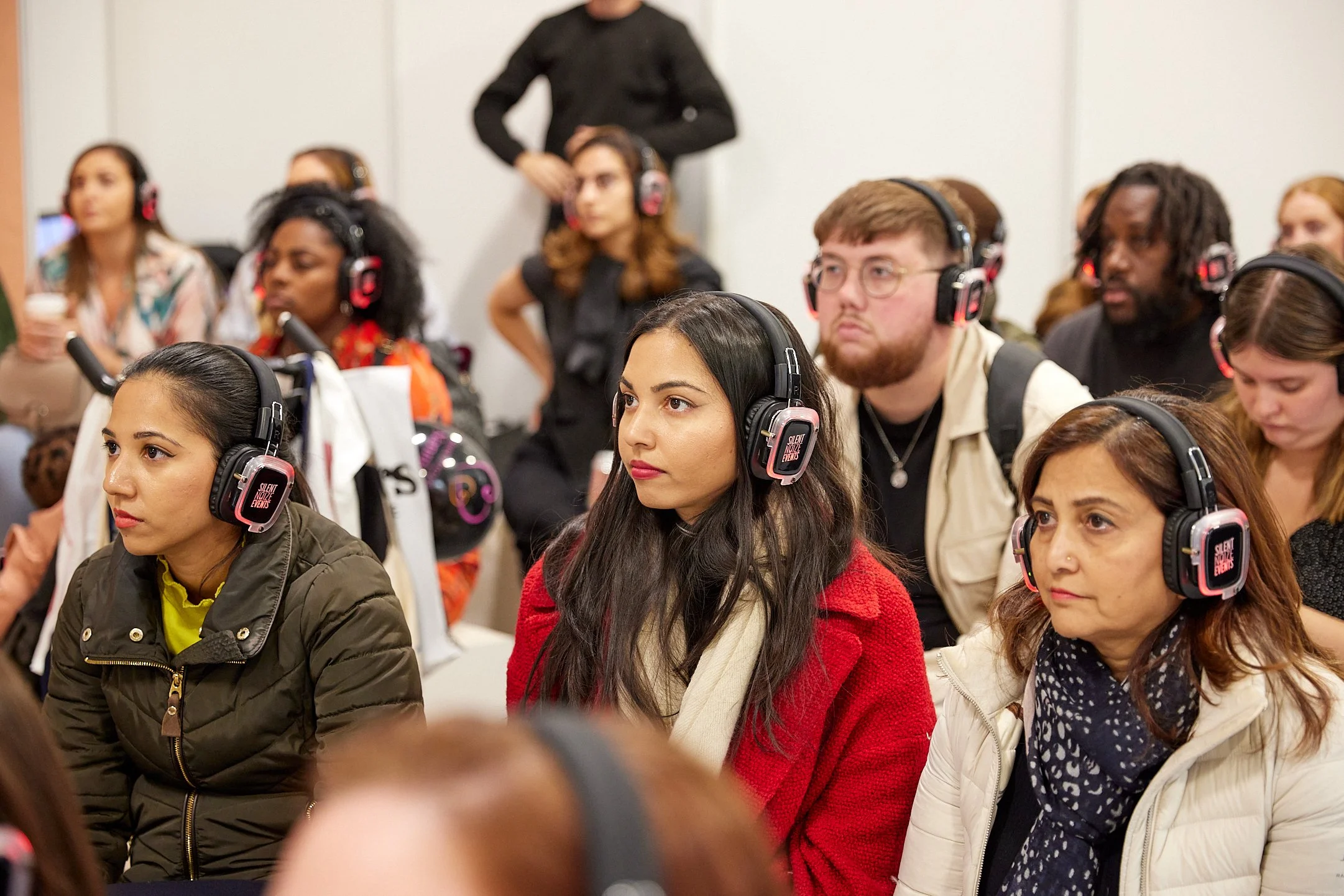 A group of attendees at a conference, all wearing black and pink headphones, seated and listening attentively.