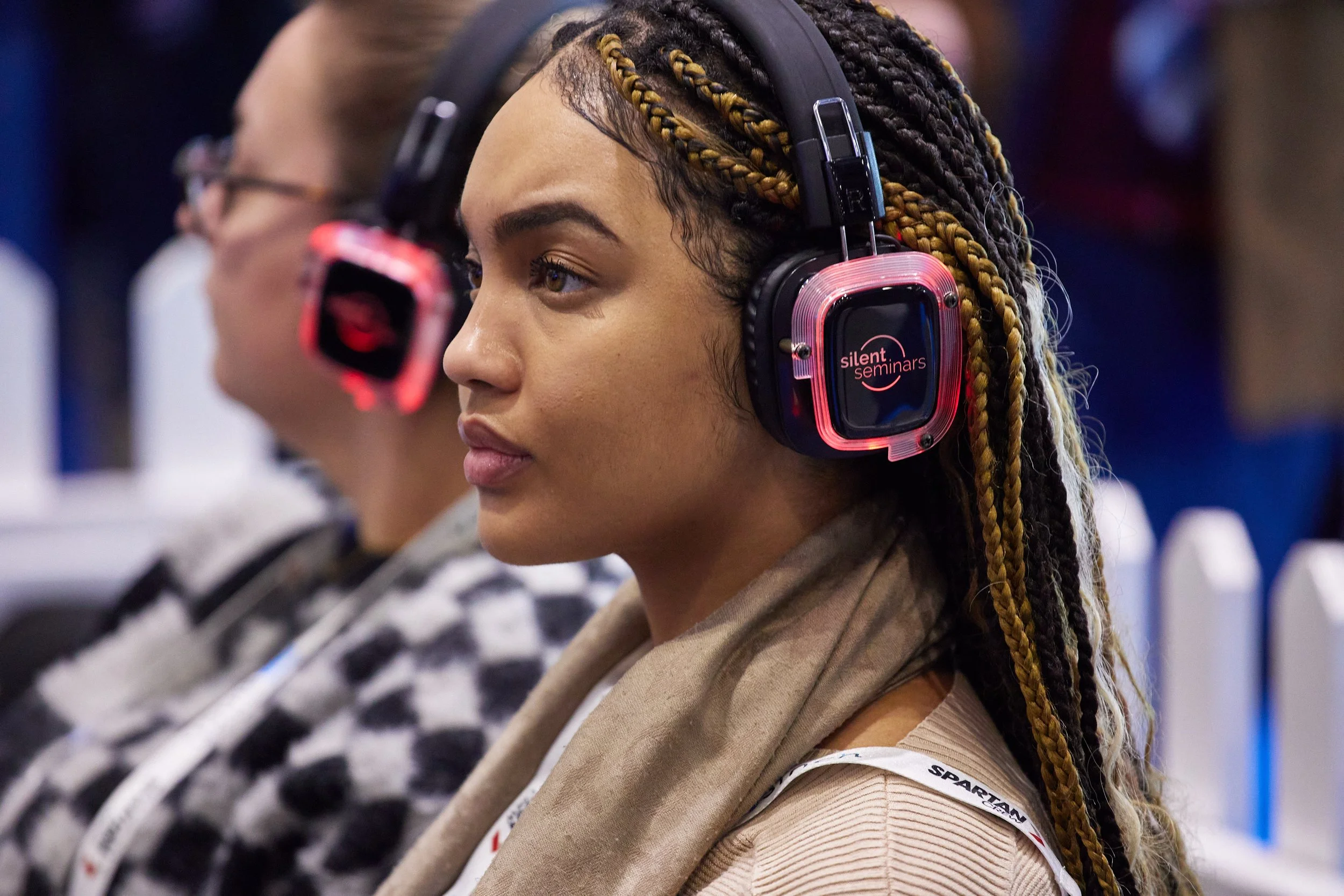 A woman with braided hair and tan skin wearing large black headphones with pink accents and a logo that reads 'silent seminars' at an indoor conference or event.