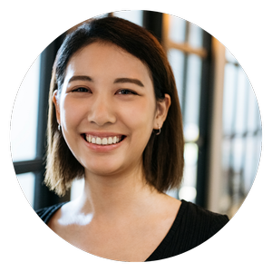 Portrait of a young woman smiling indoors with large windows in the background.