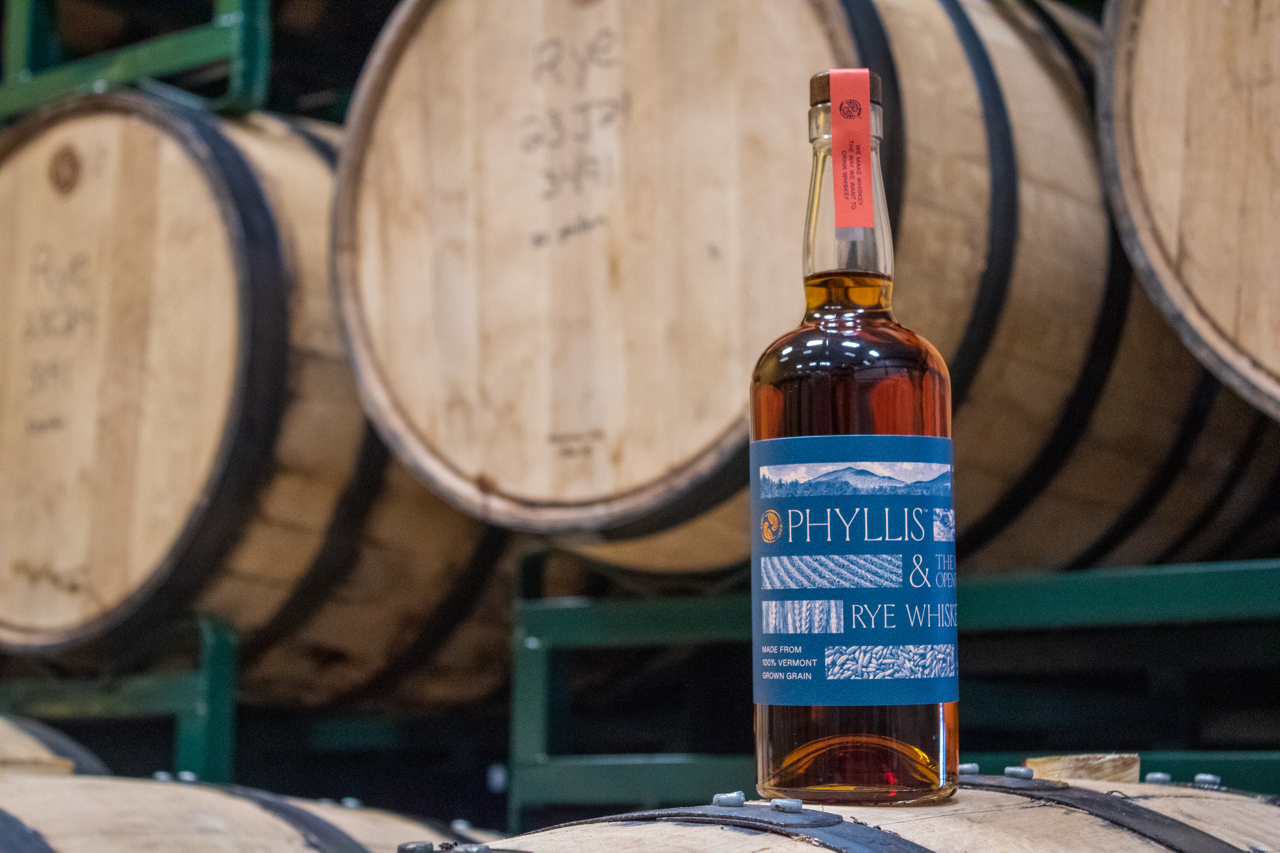 Phyllis Whiskey bottle in a barrel room with barrels of whiskey in the background.