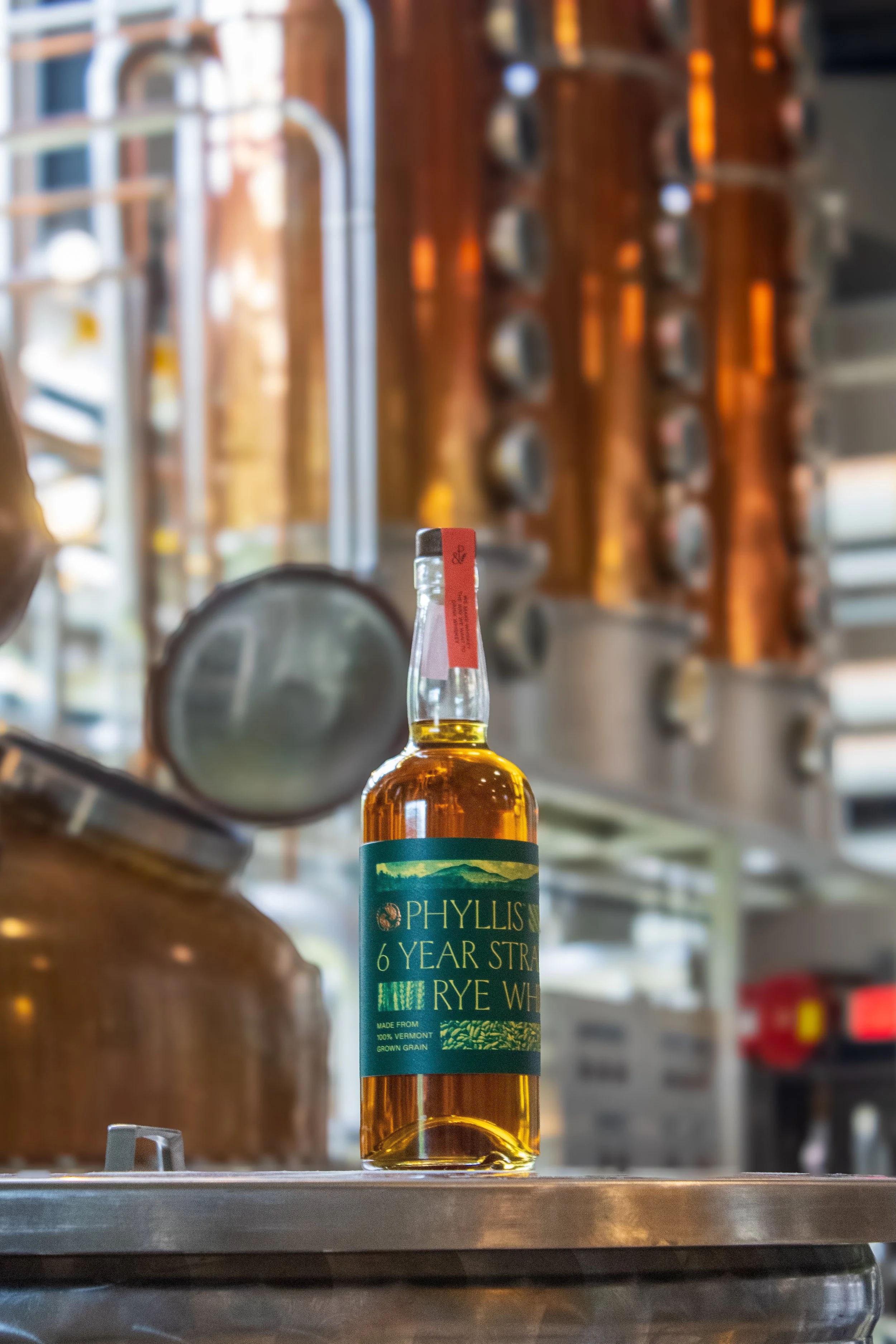 A bottle of Phyllis 6 Year Rye Whiskey sitting in front of a copper whiskey still.