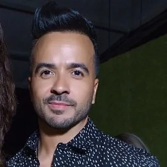 Man with styled hair and a black patterned shirt against a dark background