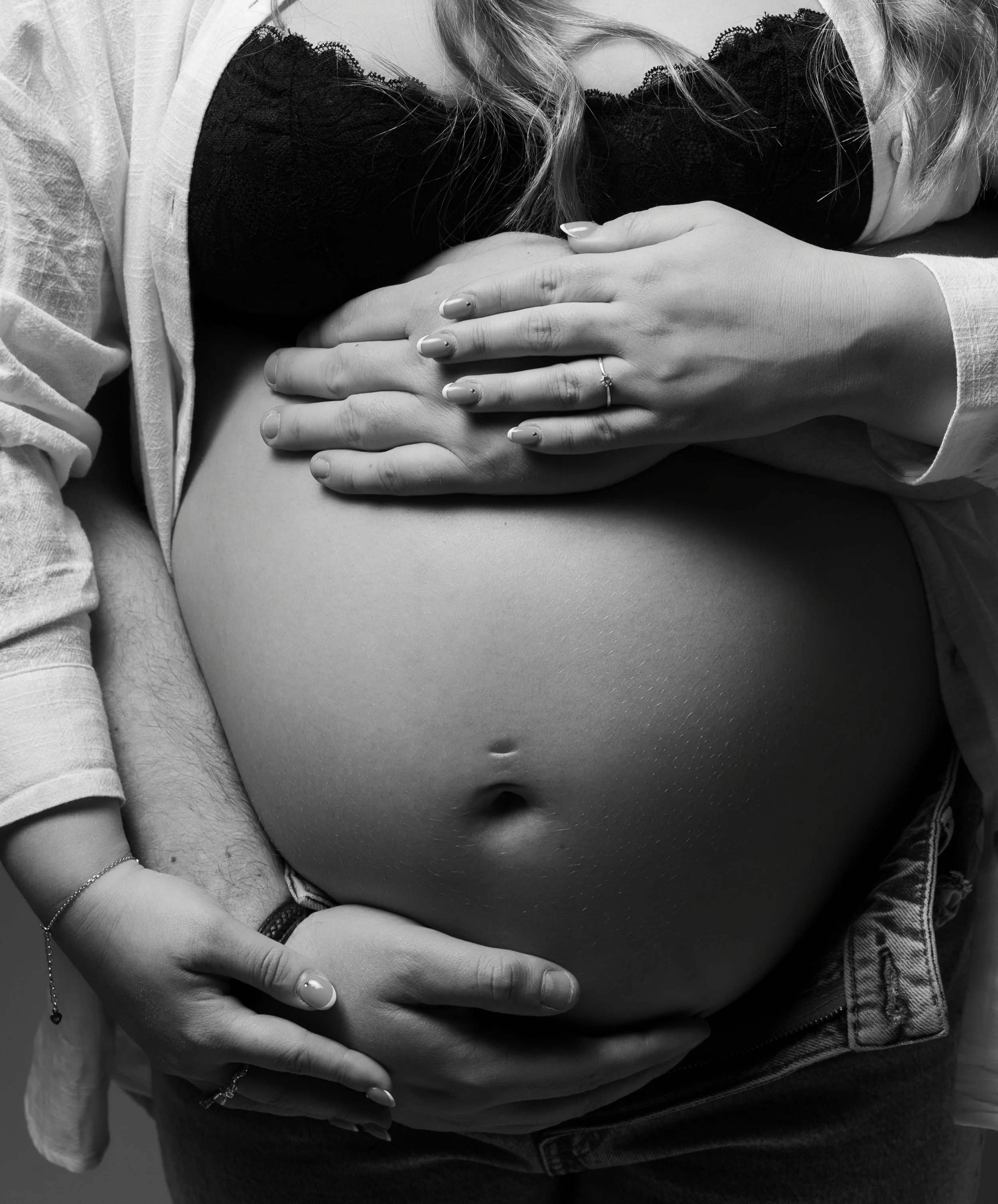 Nærbilde av en person med lang blond hår som holder sine egne håndflate oppå mageområdet. Gravidfotografering i Fredrikstad, Østfold.