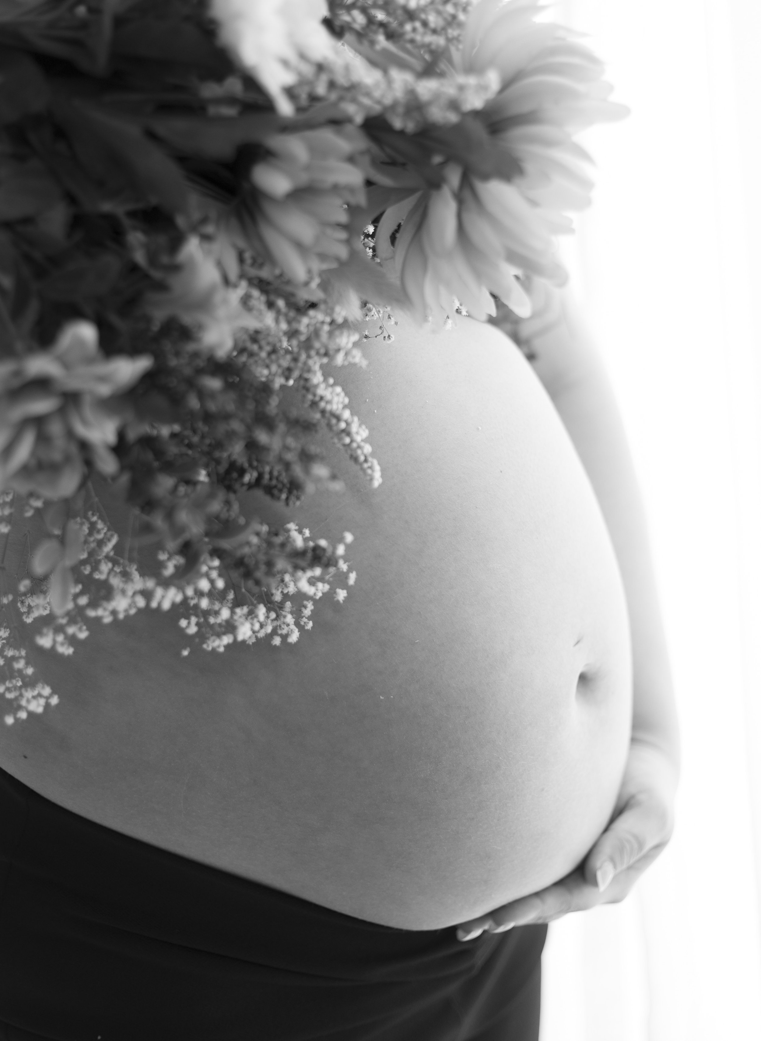 Nærbilde av en gravid kvinnes mage, med blomsterdekorasjon på magen, i svart og hvitt. Gravidfotografering i Fredrikstad, Østfold.