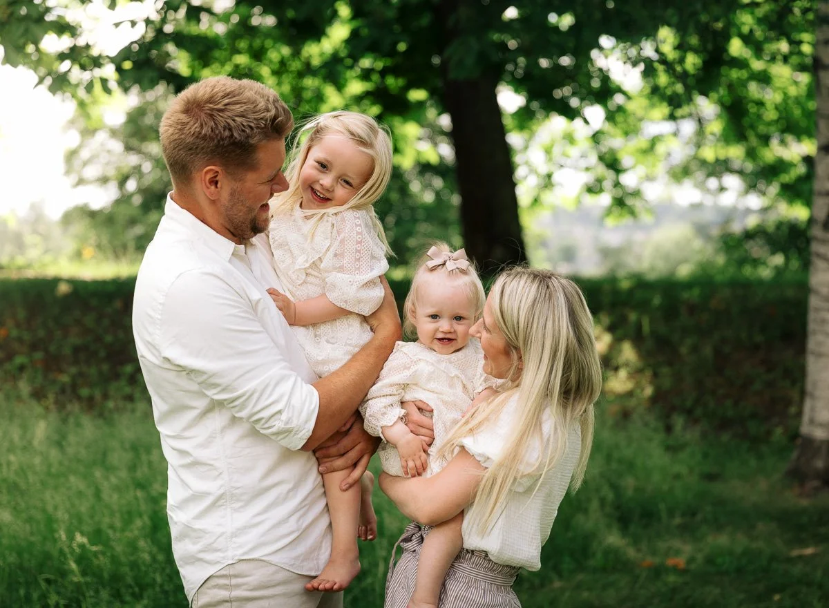 Familiefotografi av mor, far og to jenter i idylliske omgivelser.