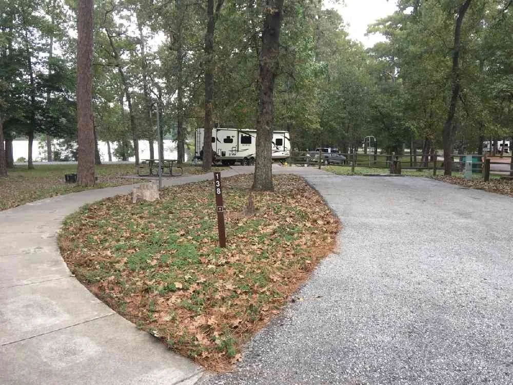 A parking lot at a campground with a RV, trees, and a lake in the background.