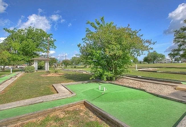 Miniature golf course with green putting area, trees, and a partly cloudy sky.