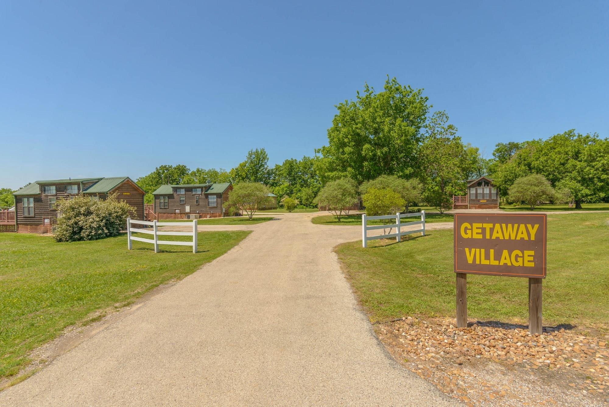 Pathway leading into Getaway Village with wooden cabins and trees on both sides and a blue sky above.