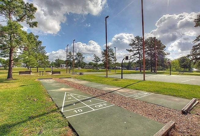 Outdoor park with shuffleboard and basketball courts, trees, cloudy sky.