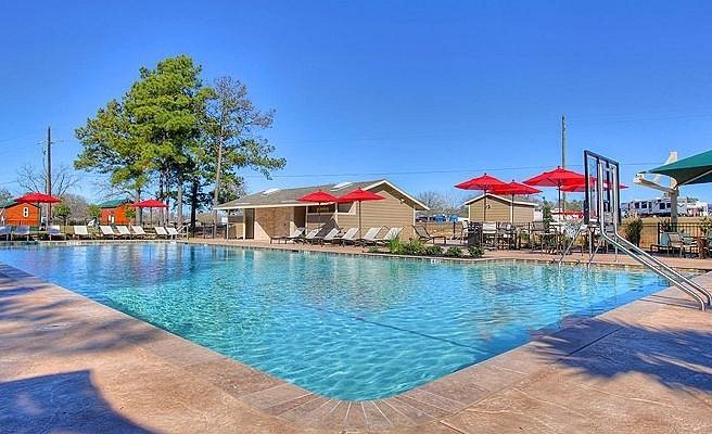 Outdoor swimming pool with lounge chairs and red umbrellas under a clear blue sky.